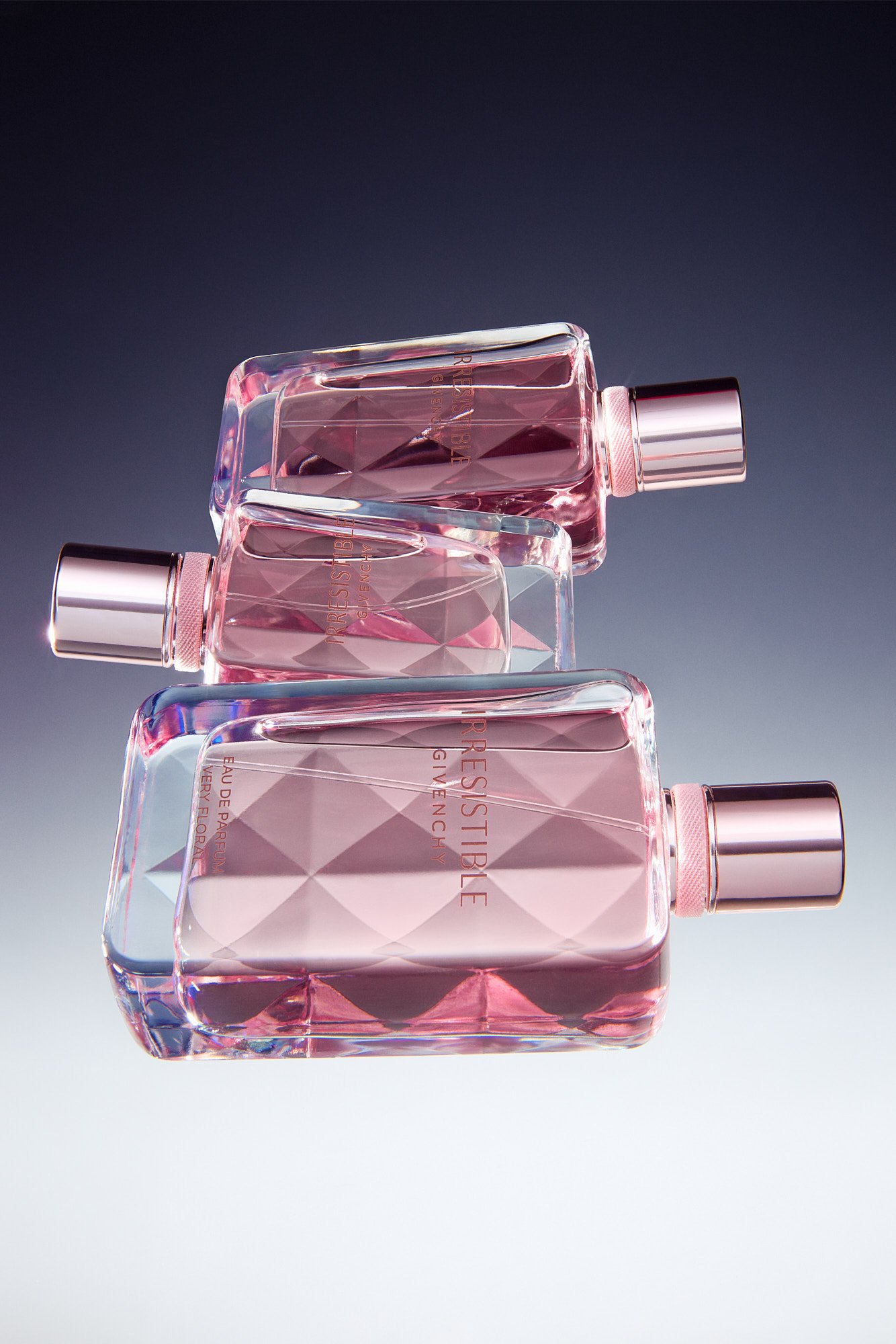 Three bottles of pink Givenchy perfume with silver caps arranged in a staggered formation against a gradient background.