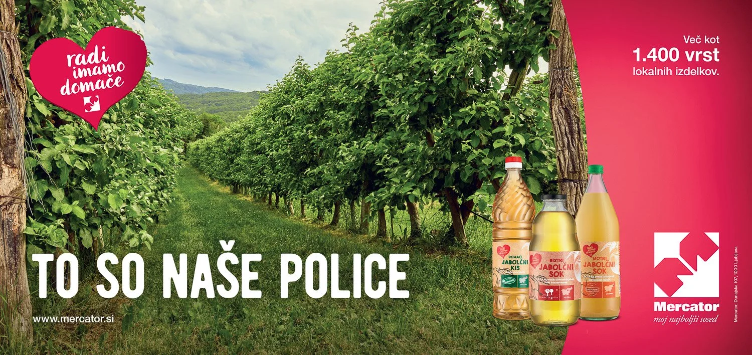 An advertisement for Mercator featuring a lush green orchard with rows of trees, and three bottles of apple juice and apple cider on the right side, with the brand's logo and slogan in Slovenian.