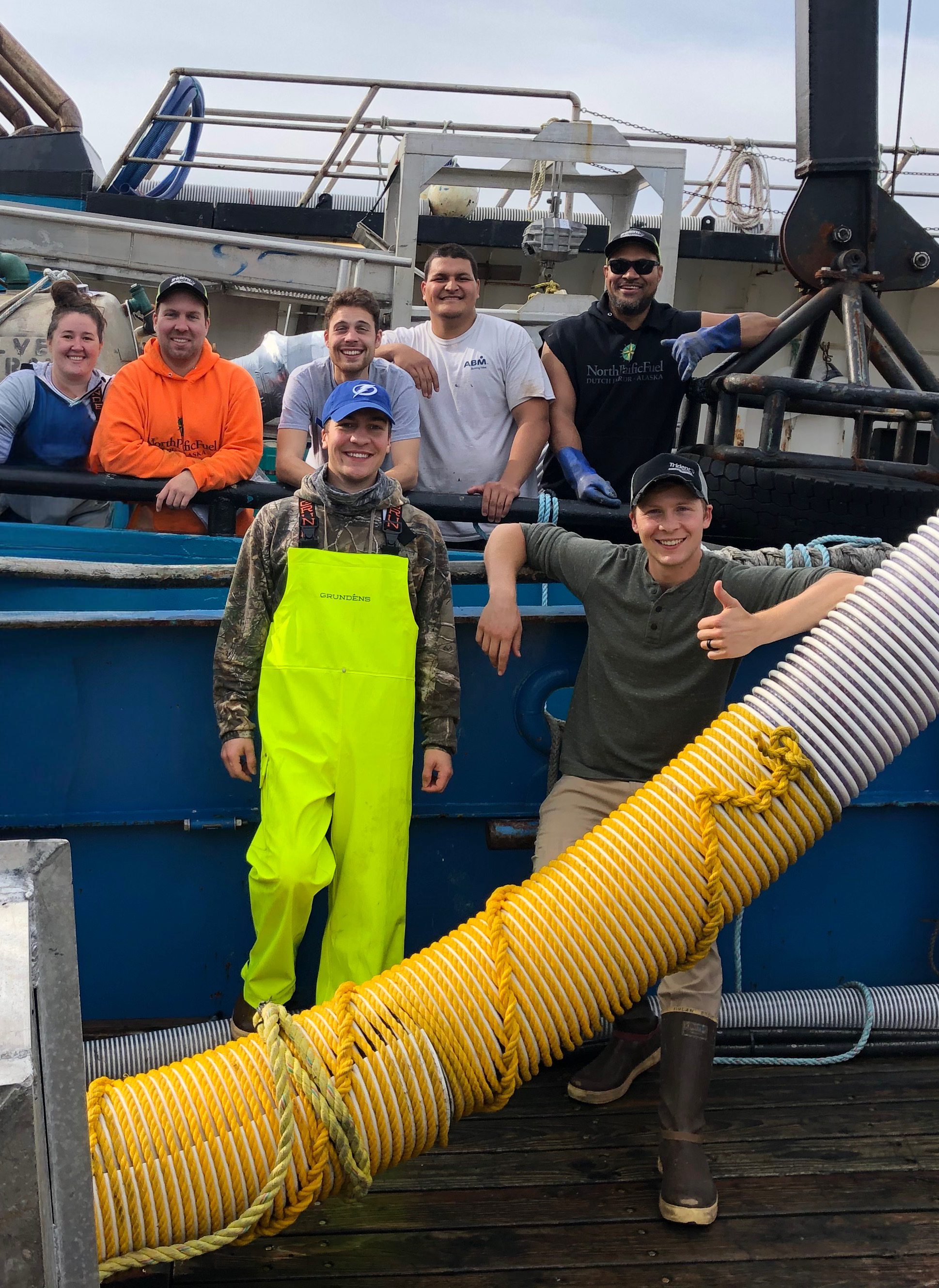 Group of eight people posing on the F/V Silver Spray, with some wearing work gloves, waterproof boots, and bright yellow and orange safety gear.