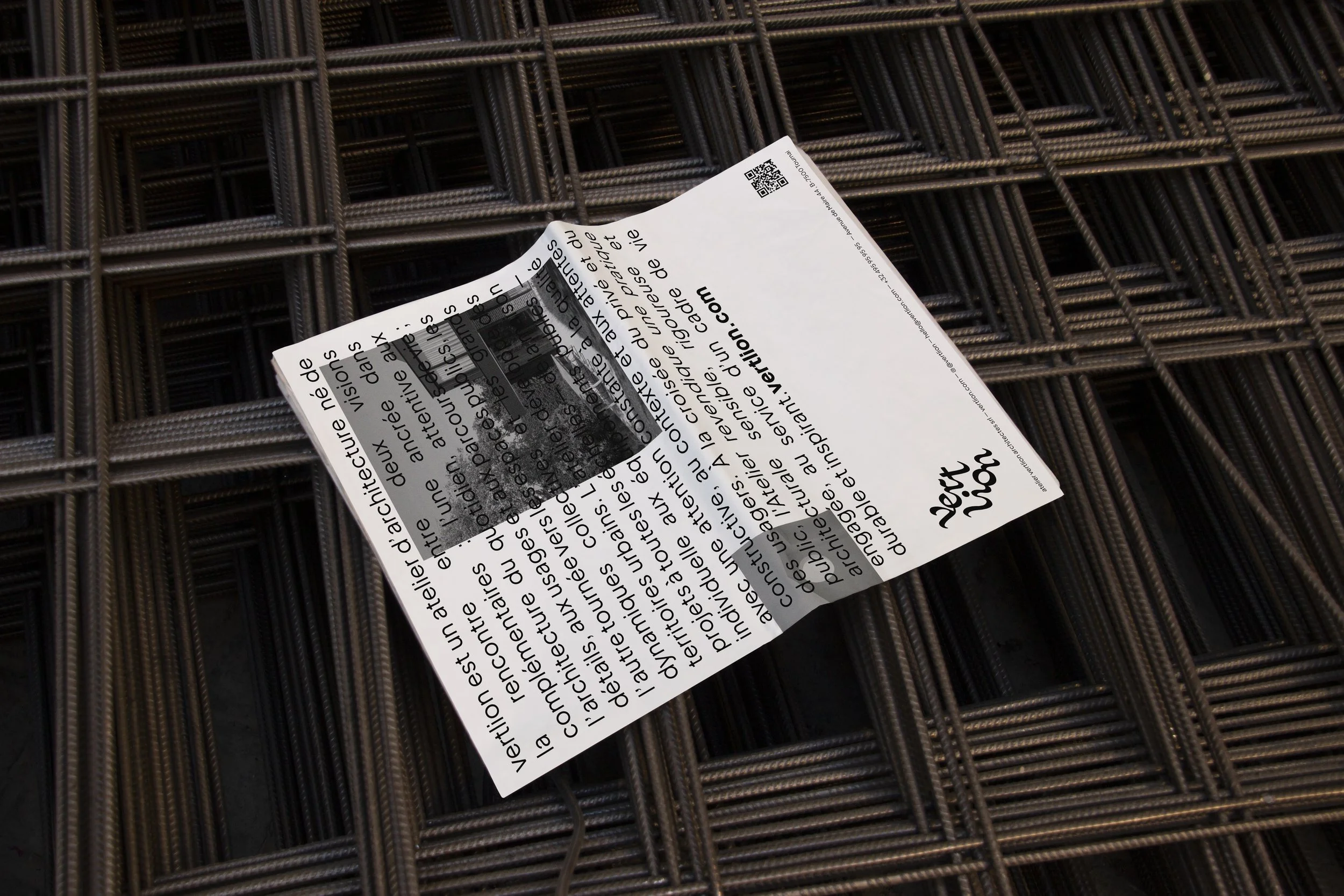 Une feuille de papier blanc avec du texte en français, posée sur une grille métallique. La feuille est légèrement pliée avec un coin supérieur qui dépasse.