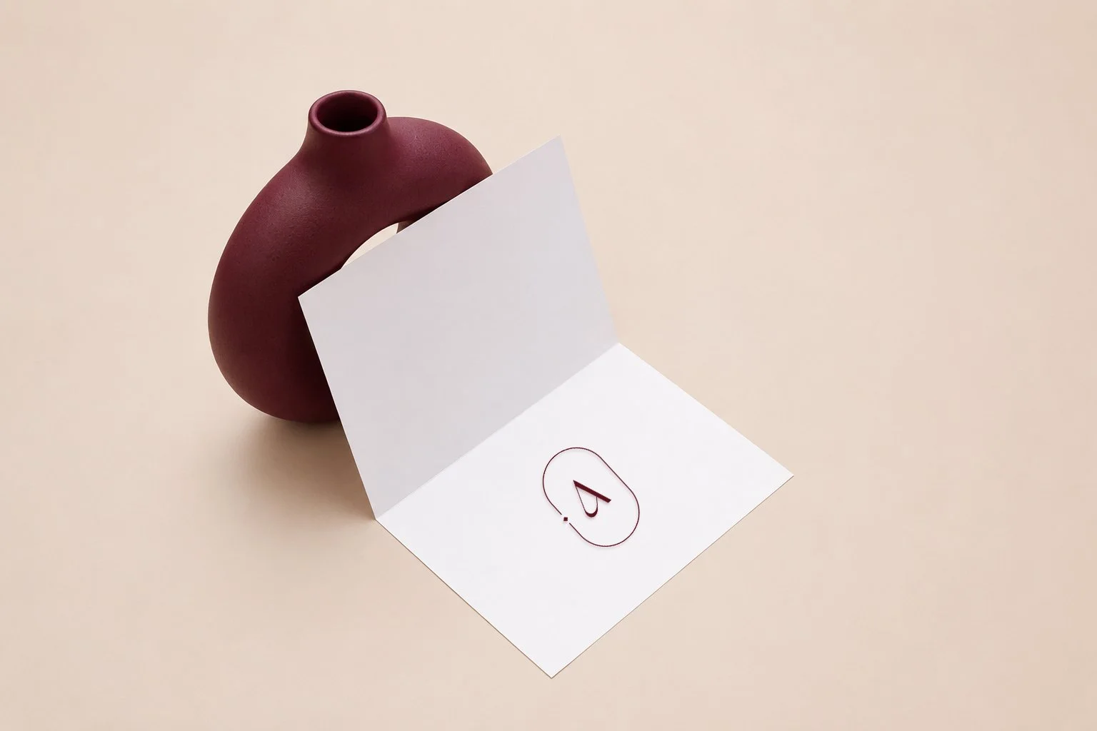 A burgundy ceramic vase with a round body and narrow neck, positioned behind an open white card or booklet with the number 4 written inside a red oval outline.