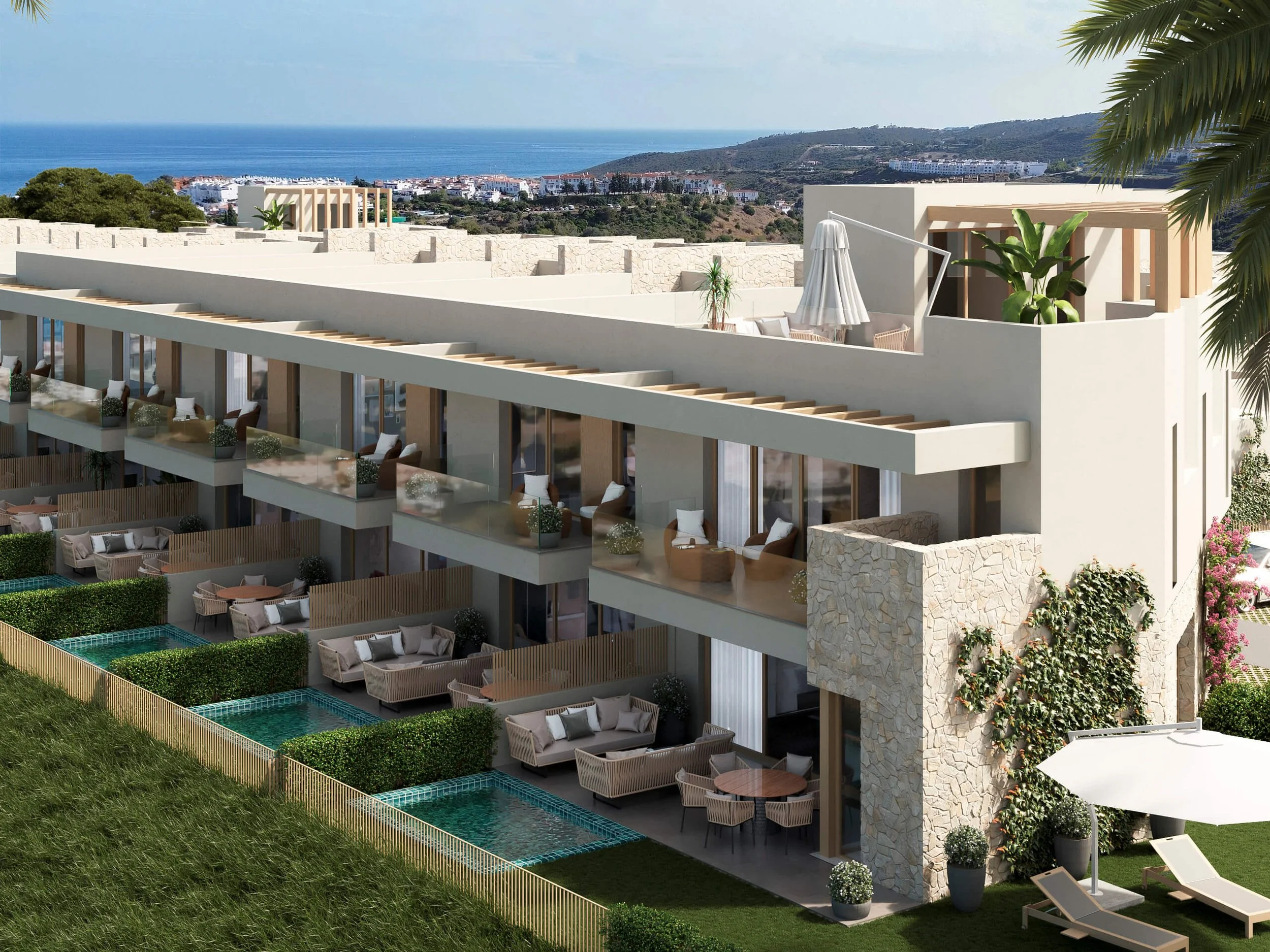 Luxury apartment building with outdoor seating and small pools, overlooking the ocean and hills, with palm trees and flowering bushes in the foreground.