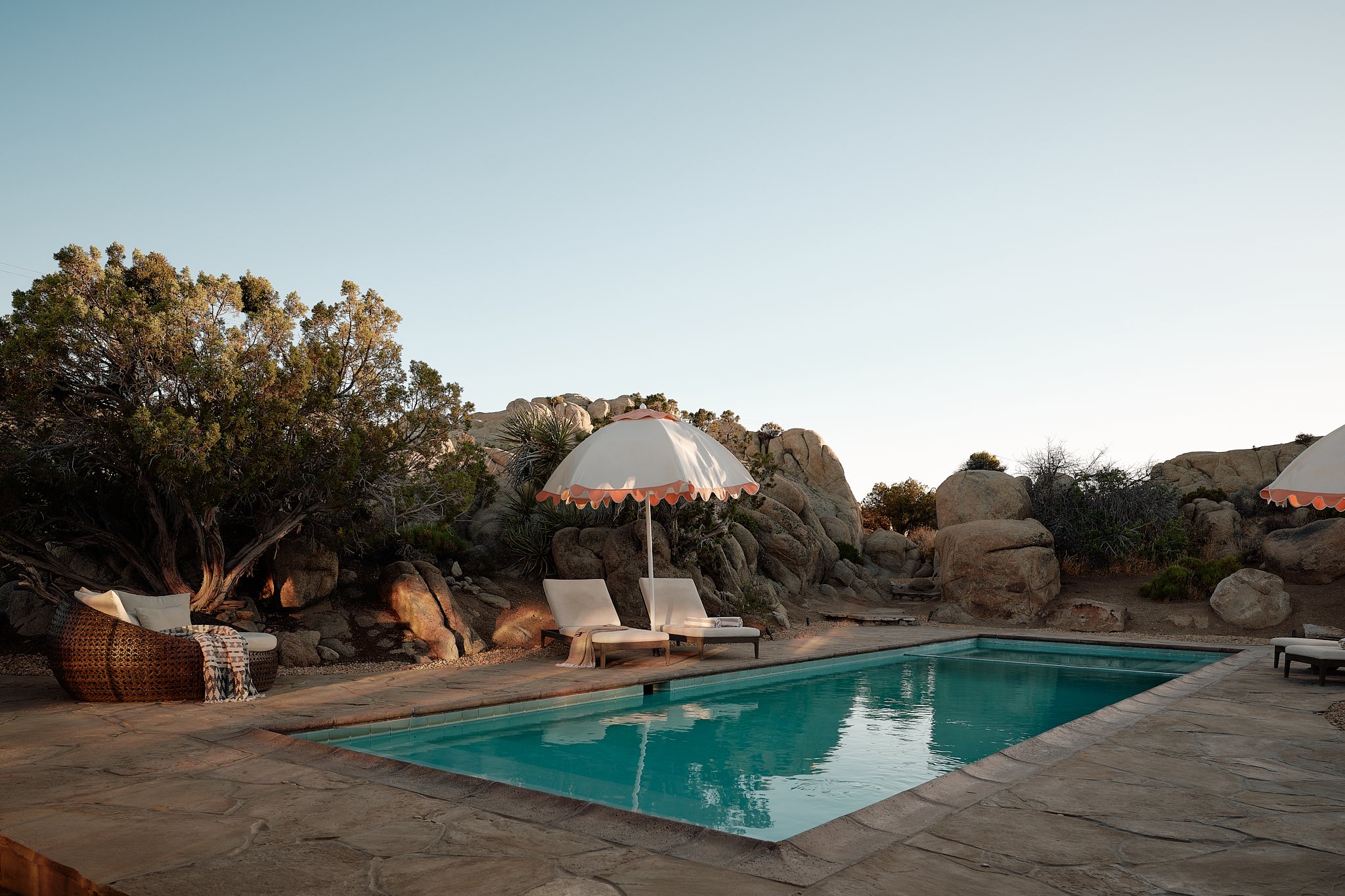 A swimming pool surrounded by lounge chairs, umbrellas, and natural rocks with desert vegetation.