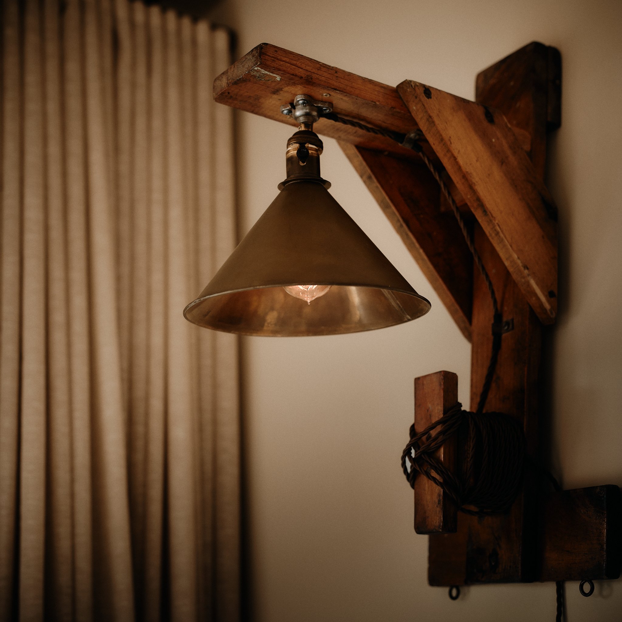 A wall-mounted lamp with a metal shade attached to a rustic wooden bracket.