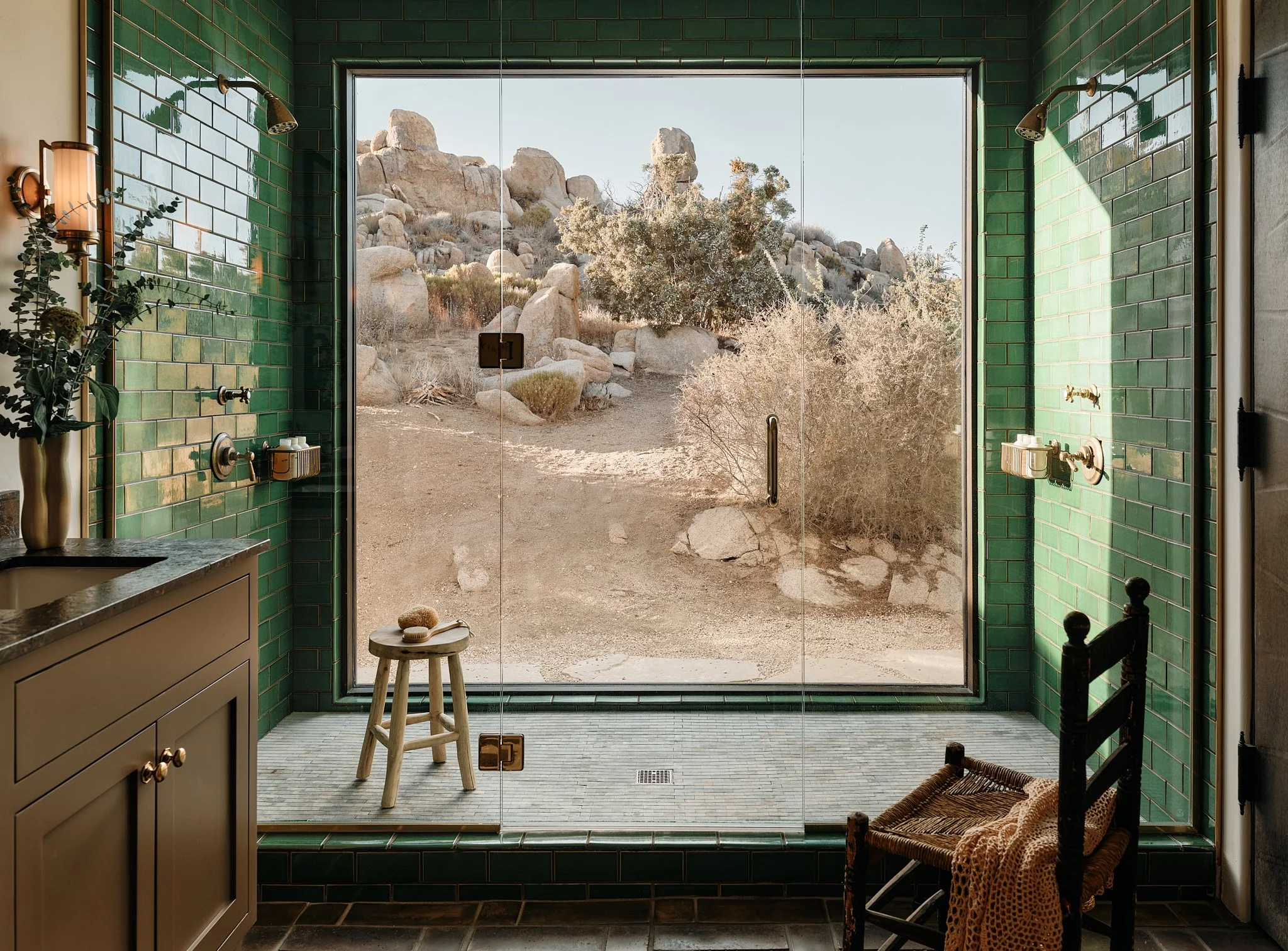 Bathroom with green tiled walls and large glass window overlooking a desert landscape with rocks and bushes.