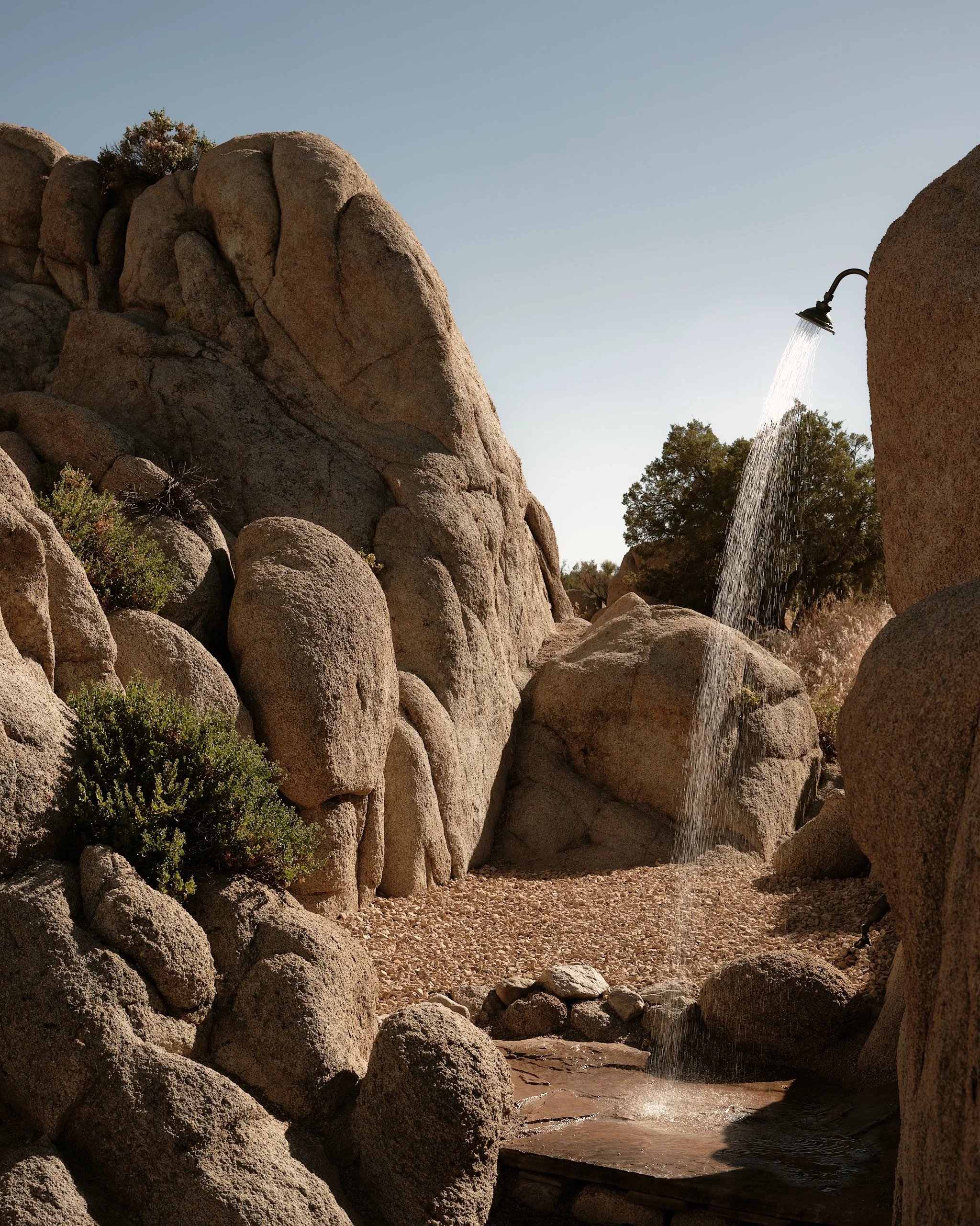 A rocky outdoor landscape with large boulders and a small waterfall with a metal shower head.
