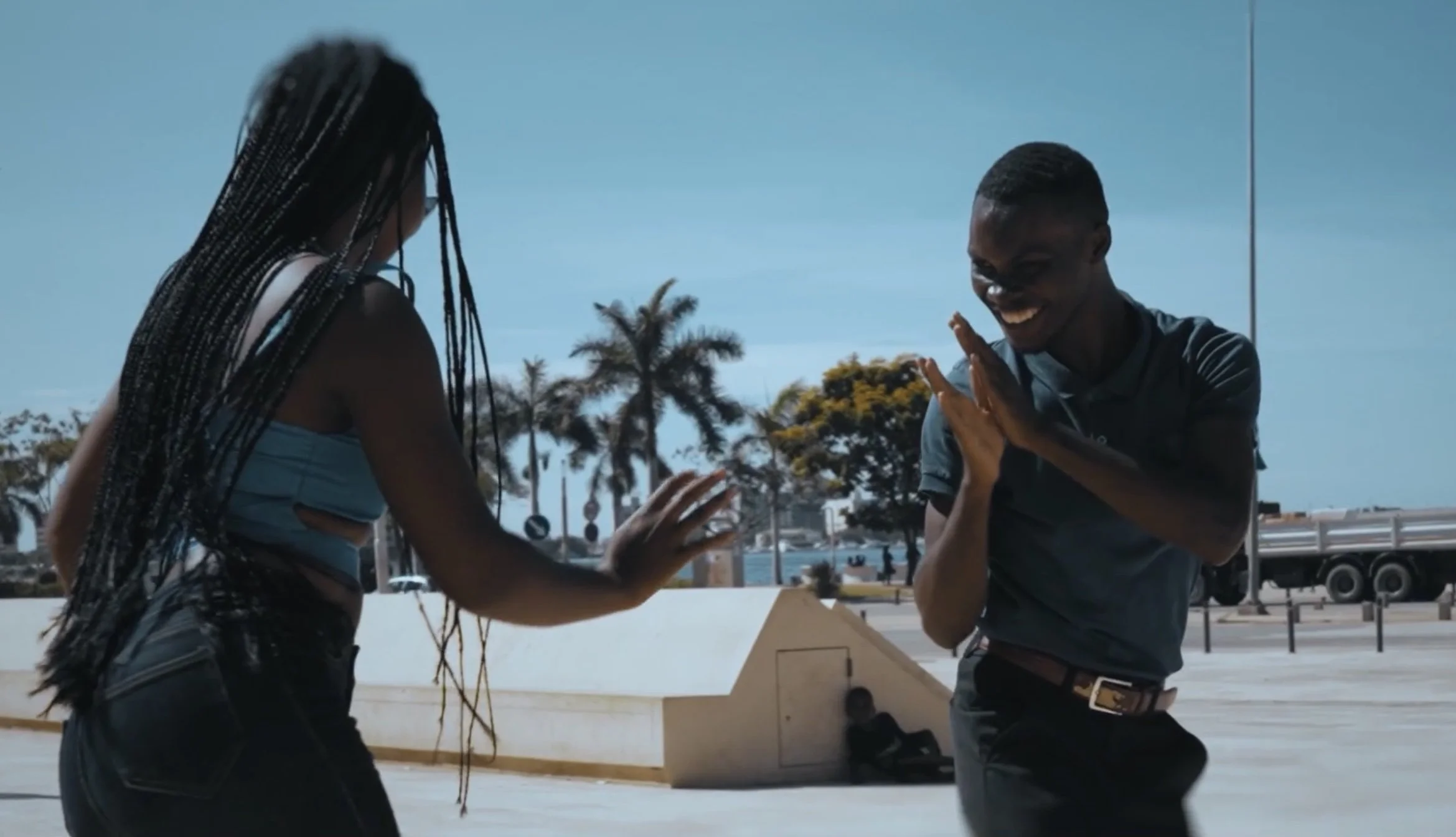 Two people dancing with palm trees and a clear blue sky in the background.