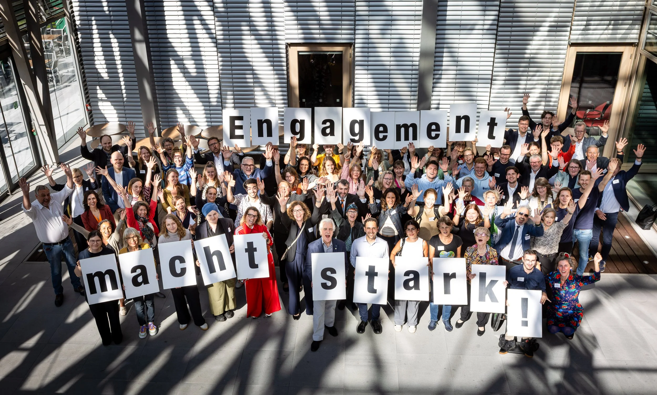 Großes Gruppenfoto von Engagierten, die gemeinsam Schilder mit dem Slogan „Engagement macht stark!" in die Höhe halten.