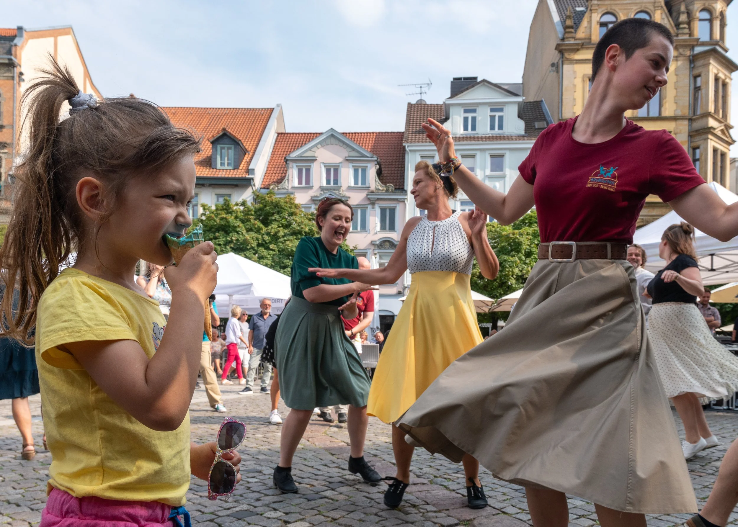 Menschen tanzen auf einem öffentlichen Platz mit historischen Gebäuden im Hintergrund.