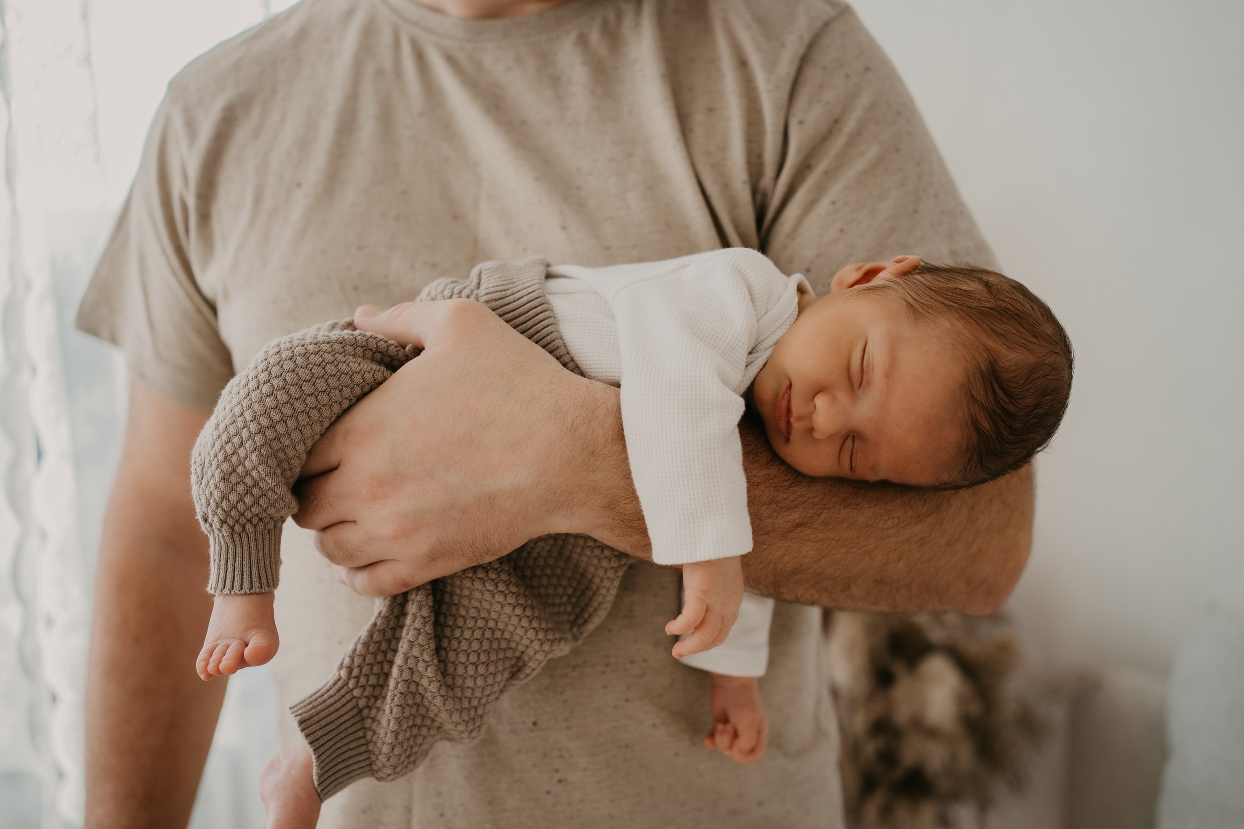 Ein Baby wird von einem Erwachsenen gehalten, während es schläft, im Innenraum mit hellem Licht.