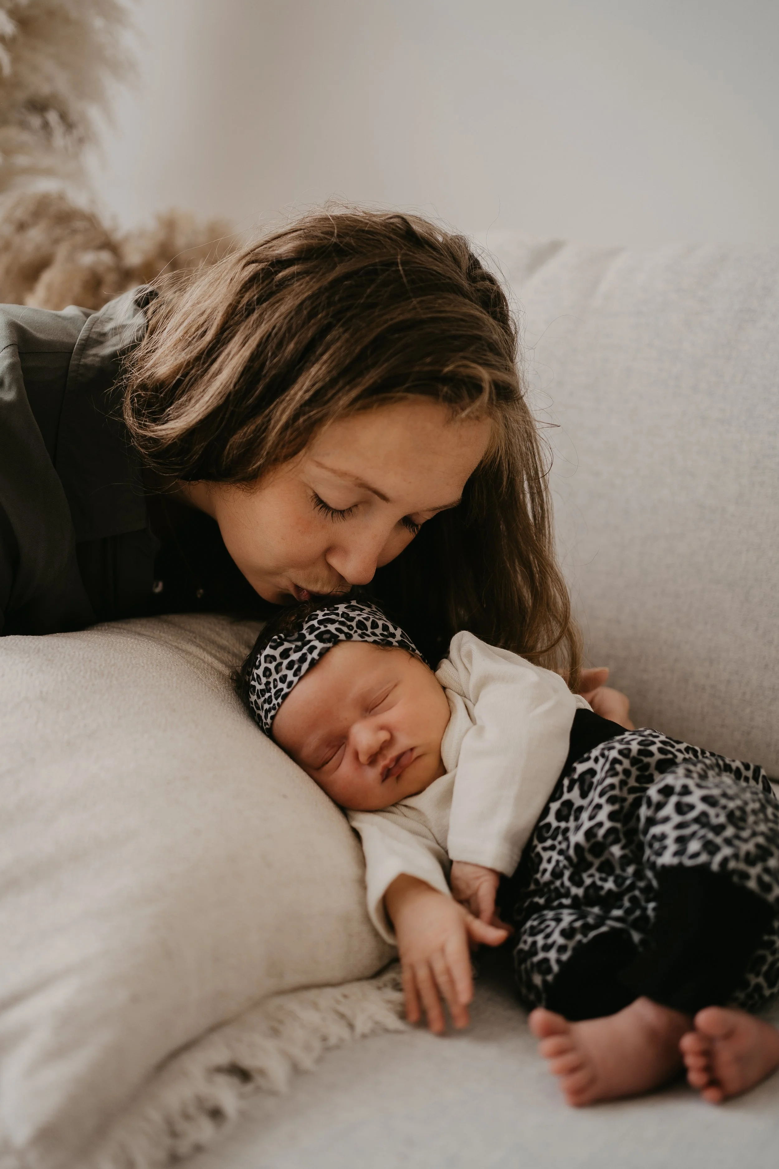 Eine Frau und ein Baby schlafen eng aneinander auf einer Couch, das Baby trägt einen Leoparden-Print-Hut und Höschen.