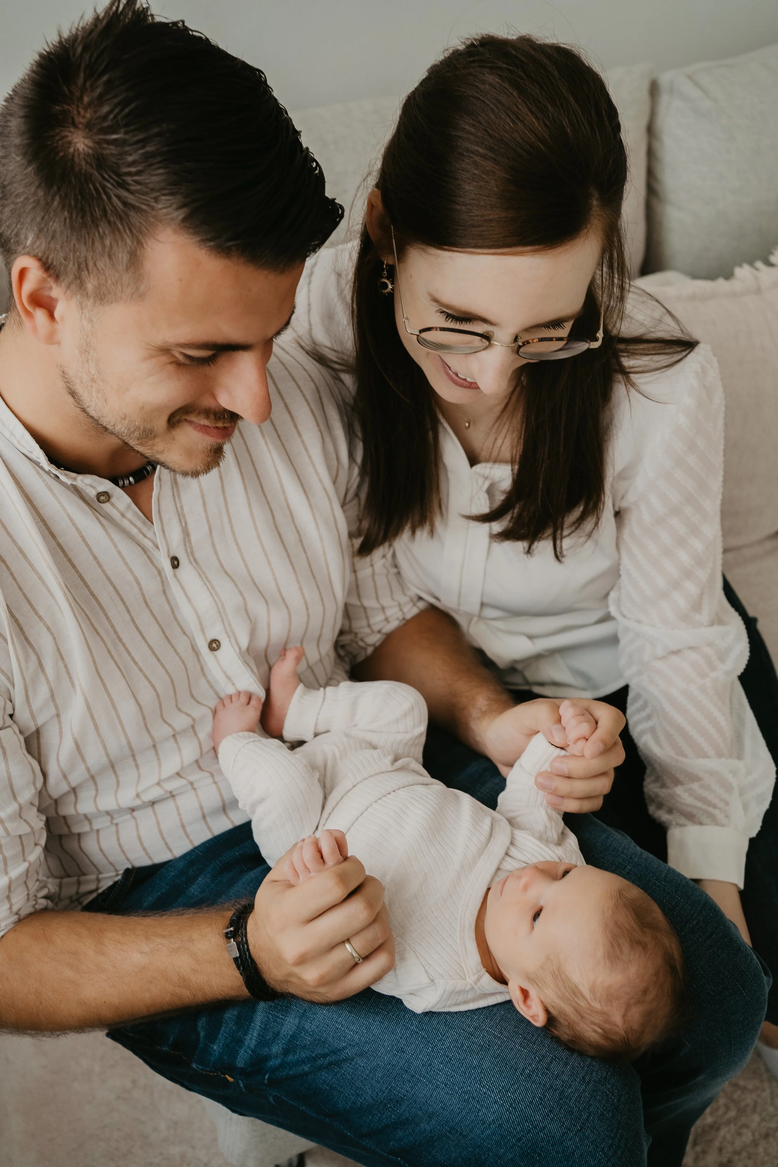 Familie mit zwei Erwachsenen und zwei Babys, die auf einem Sofa sitzen und miteinander lachen und spielen.