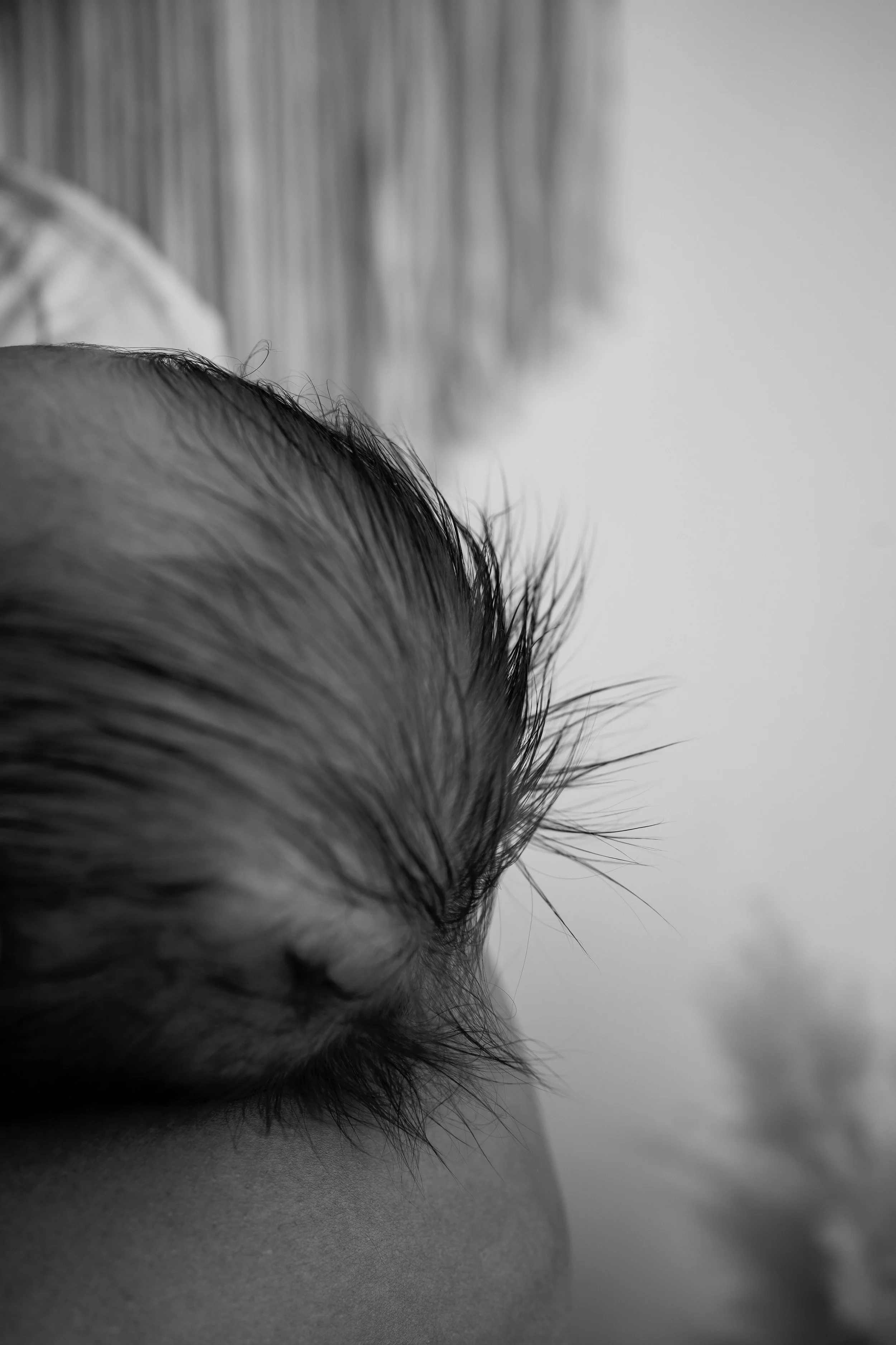 Nahaufnahme eines Babys, das auf seinem Bauch liegt, mit Fokus auf den runden Kopf und die feinen Haare, mit einem neutralen Hintergrund im Schwarz-Weiß-Stil.