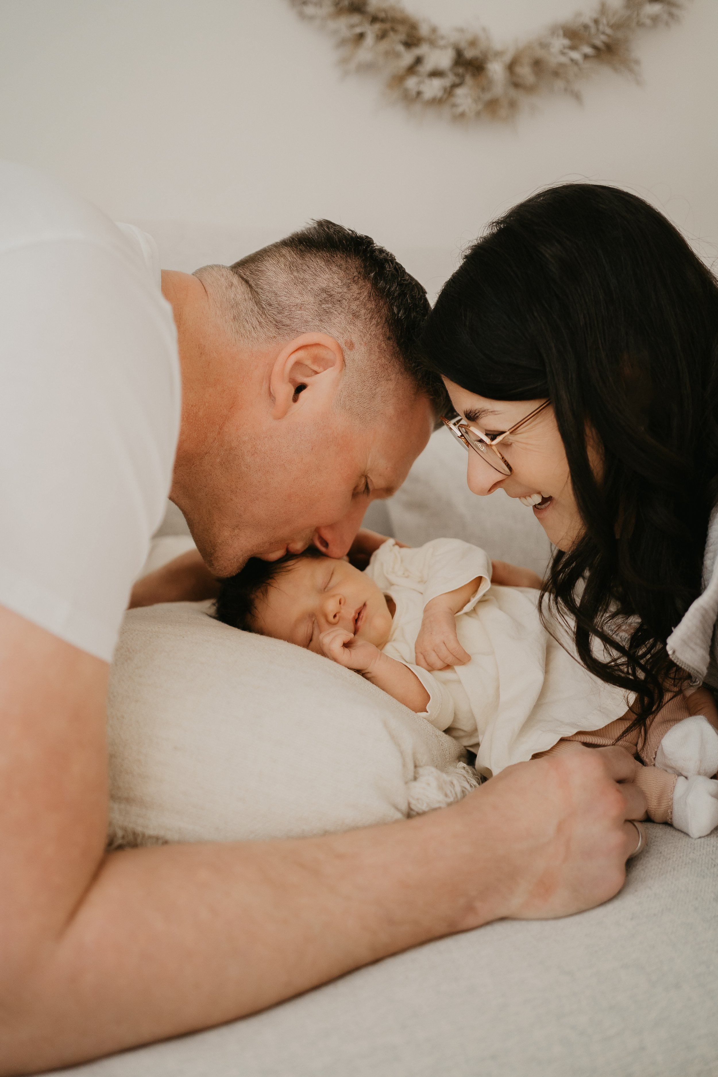 Ein freudiges Paar, ein Mann und eine Frau, lächeln glücklich, während sie mit einem neugeborenen Baby kuscheln, das friedlich schläft.