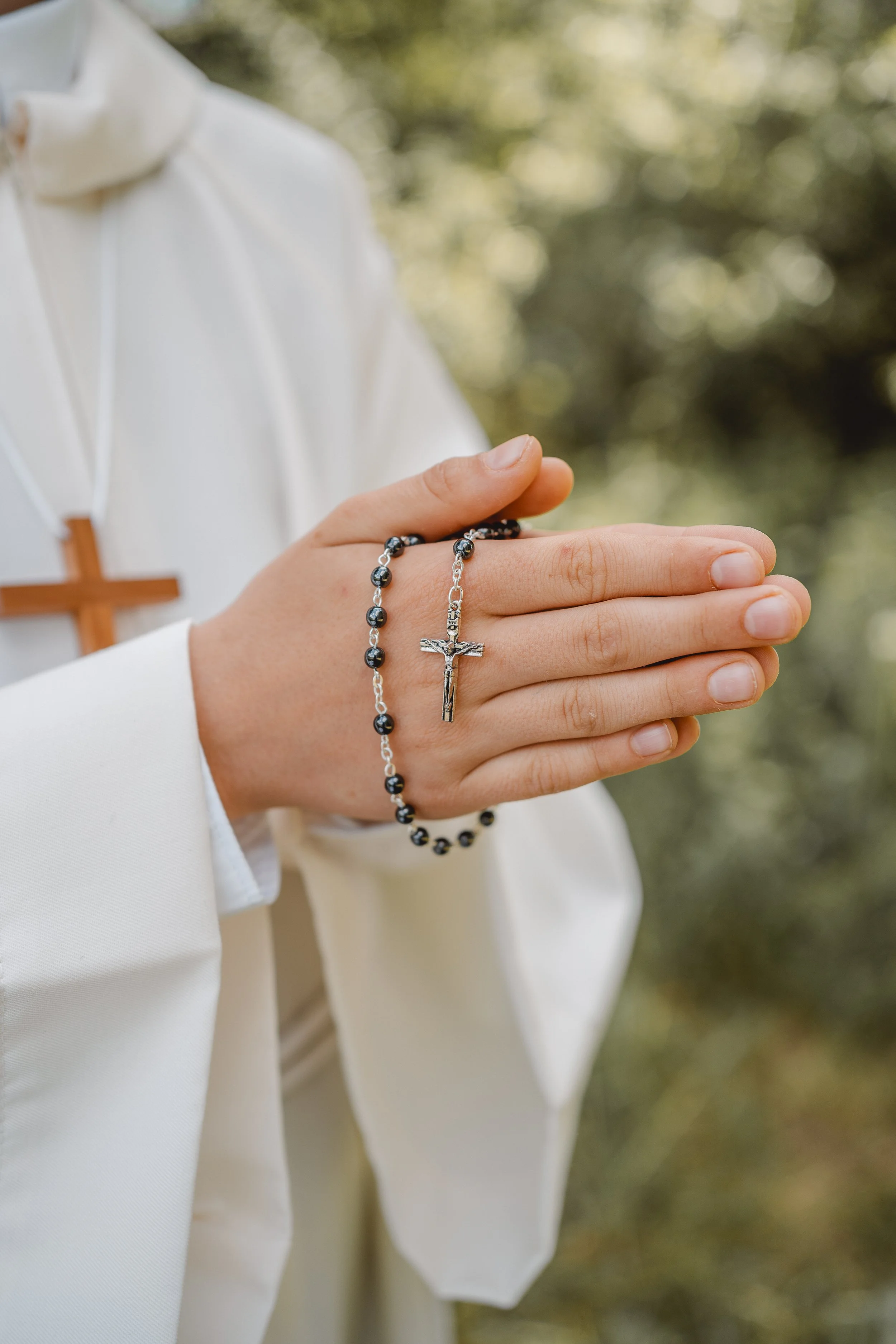 Eine Person, die ein Kreuz-Perlen-Armband mit einer Metallfigur eines Jesus-Kruzifixes hält, im Freien mit grünem Hintergrund.