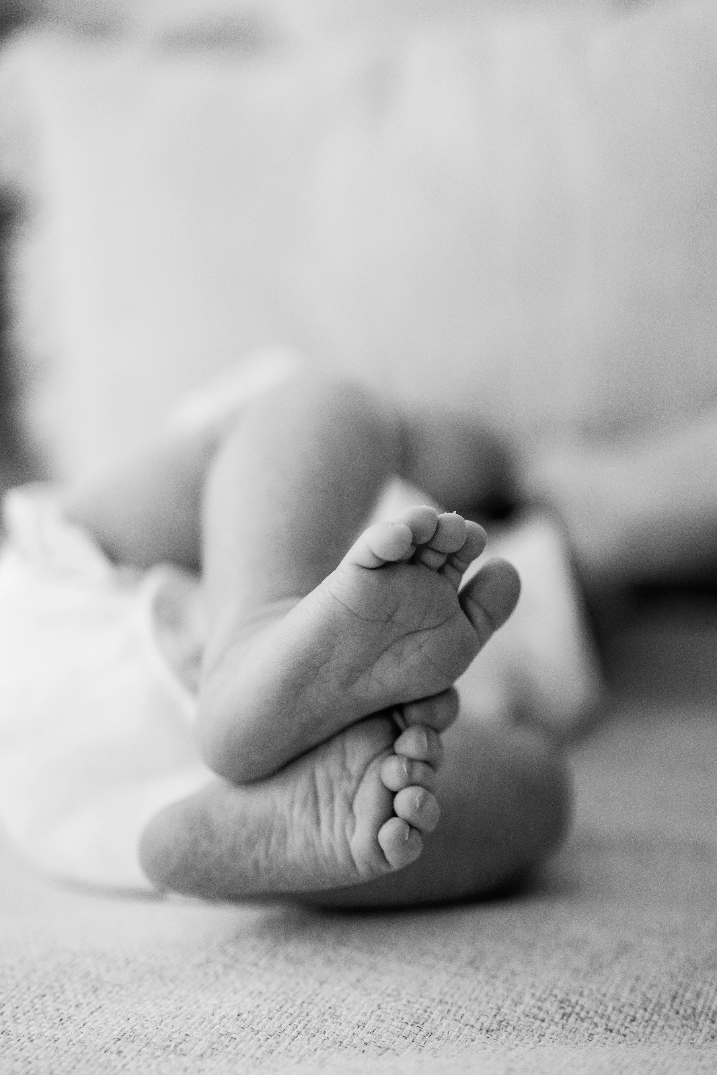 Nahaufnahme einer erwachsenen Hand, die eine kleine Kinderhand hält, im Hintergrund eine schlafende Kinderfigur, alles in Schwarz-Weiß