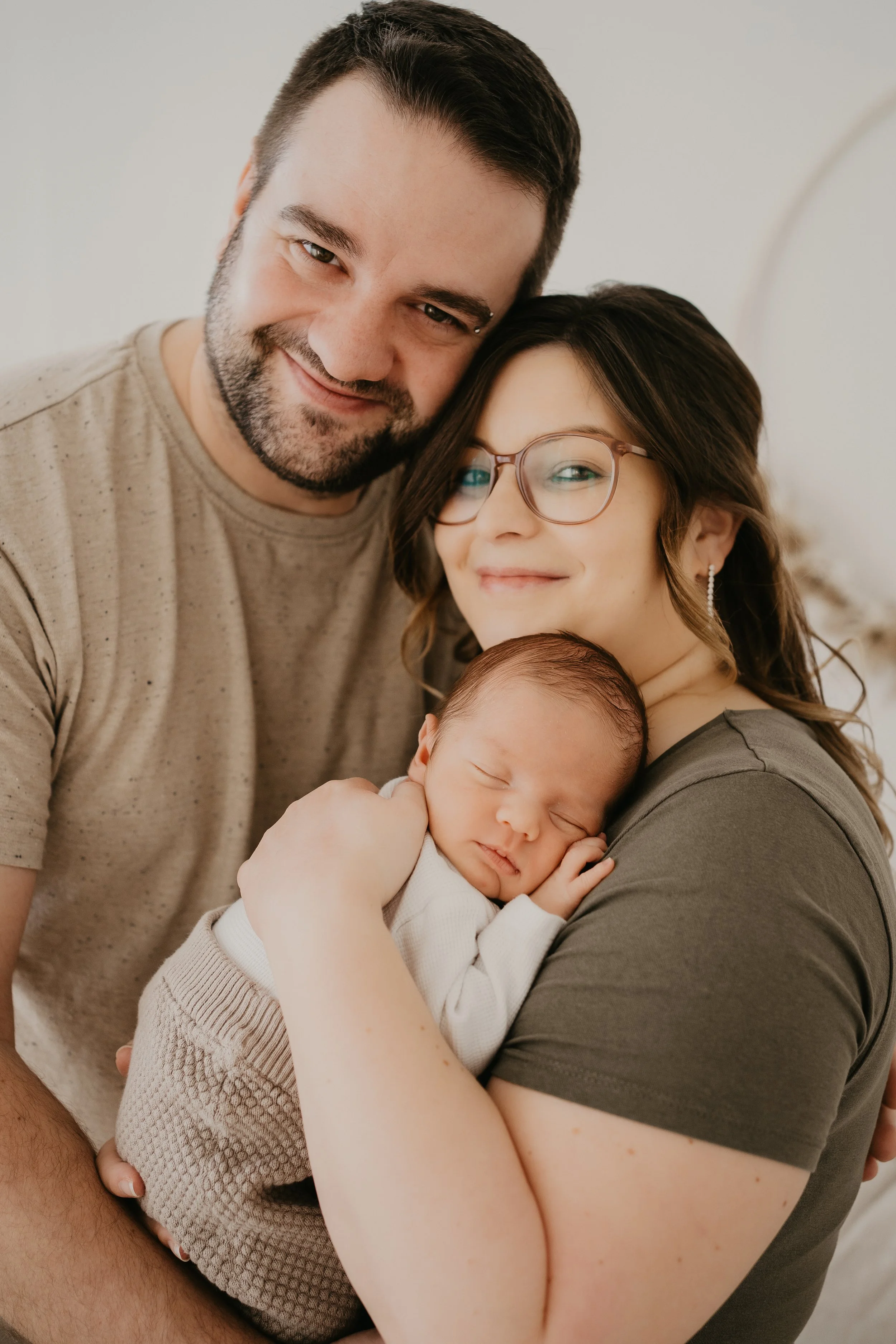 Ein glückliches Paar hält ein neugeborenes Baby im Arm, umarmt sich und lächelt.