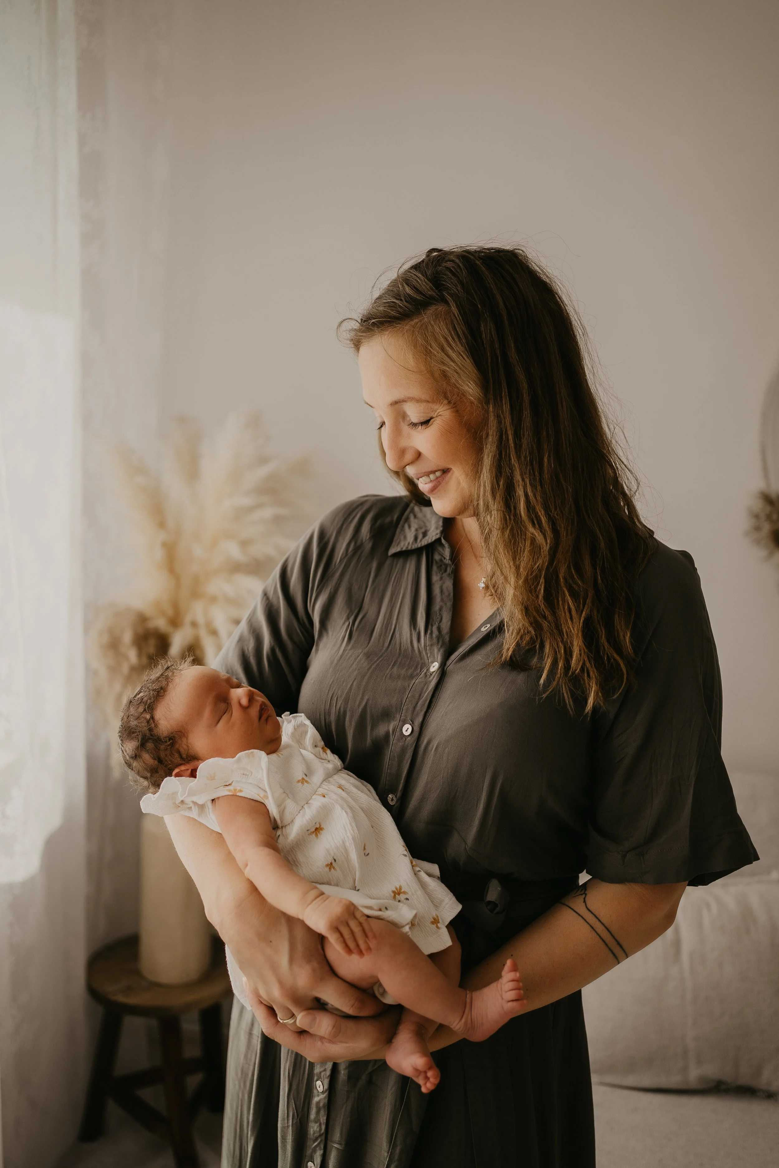 Eine Frau hält ein schlafendes Baby in den Armen, beide lächeln sich liebevoll an.