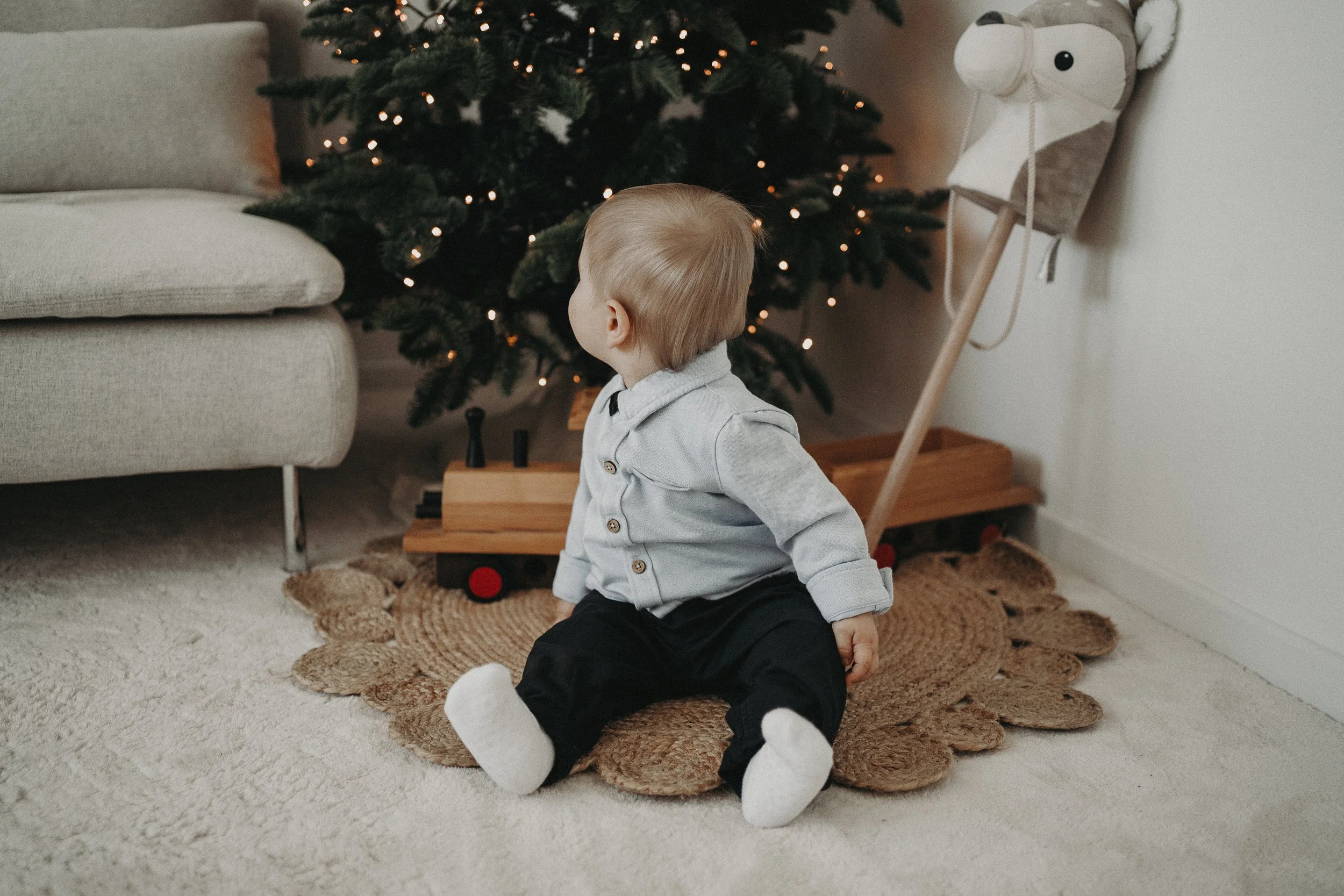 Ein kleine Junge sitzt auf einem Teppich vor einem Weihnachtsbaum mit Lichtern.