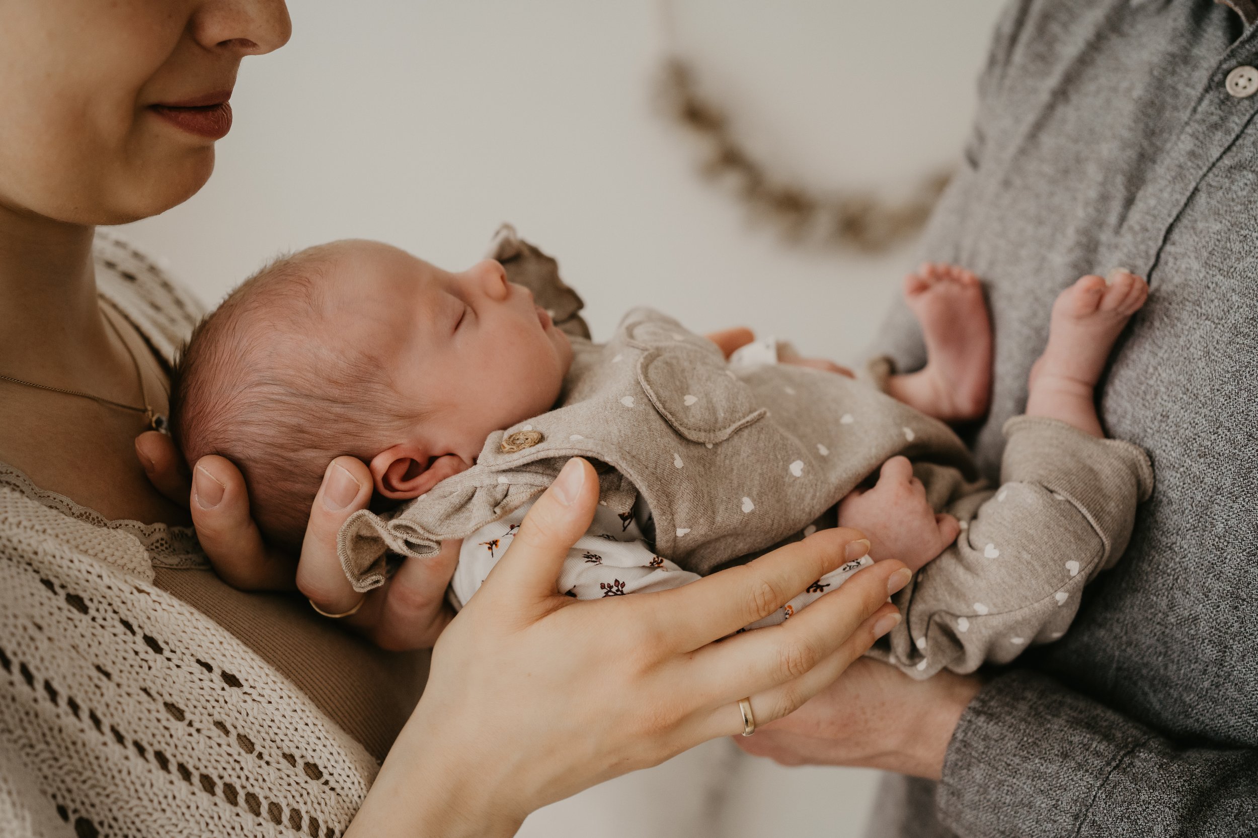 Nahaufnahme einer schlafenden Babypuppe, die von einer Frau gehalten wird, während eine andere Person, vermutlich ein Vater, den Baby trägt. Die Szene ist warm und liebevoll.
