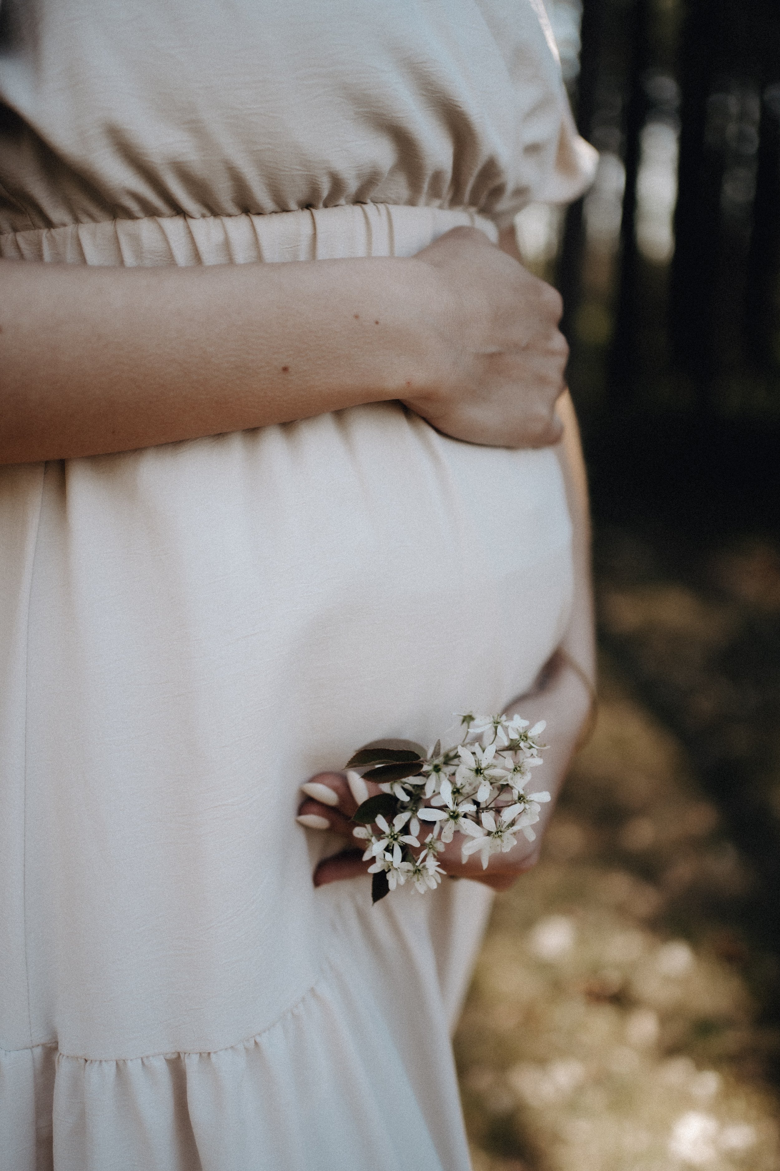Nahaufnahme einer Person, die ein weißes Kleid trägt und ein kleines Blumenbukett in der Hand hält