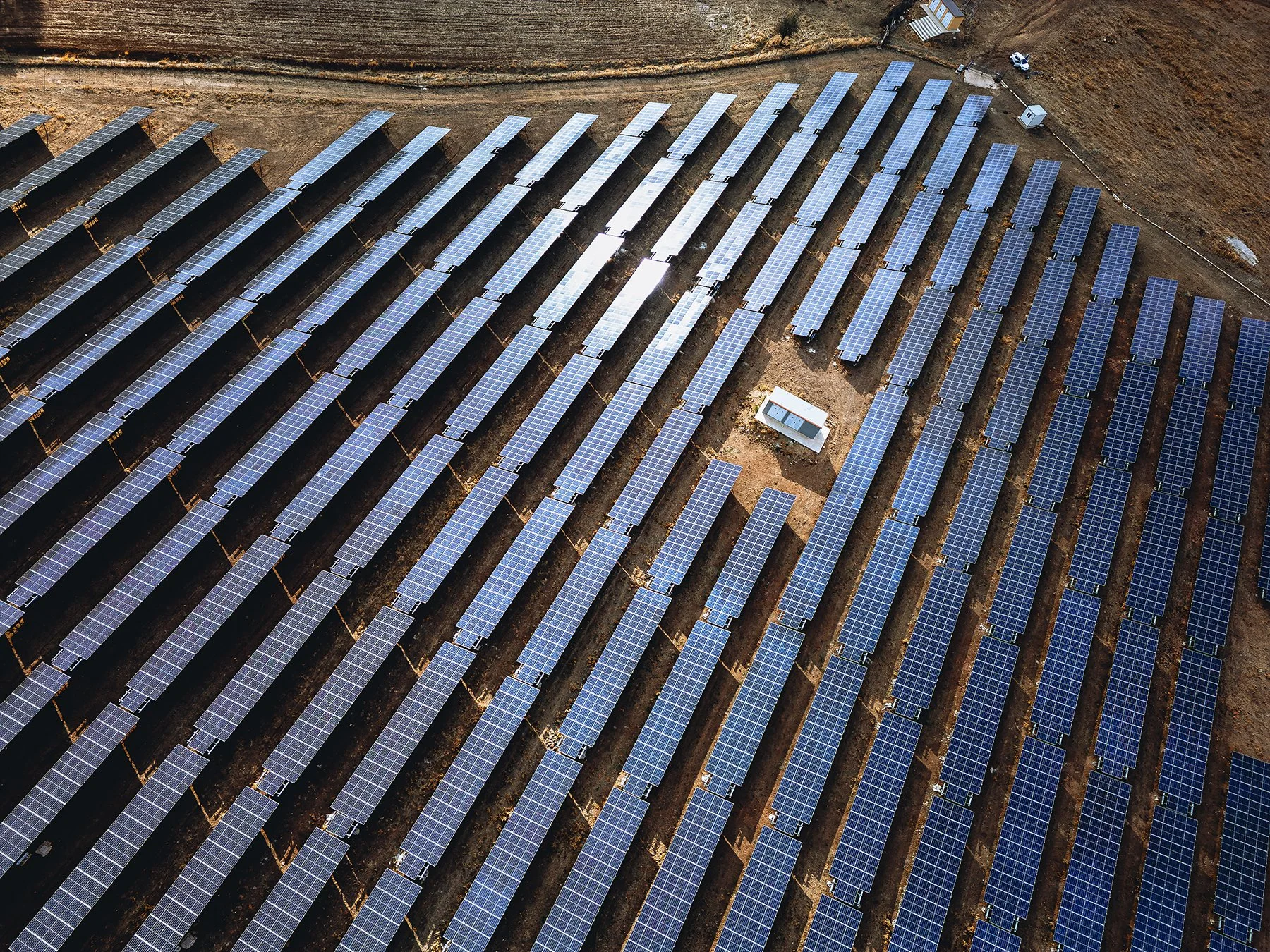 Luchtfoto van een veld met meerdere rijen zonnepanelen op een kale, glooiende ondergrond.