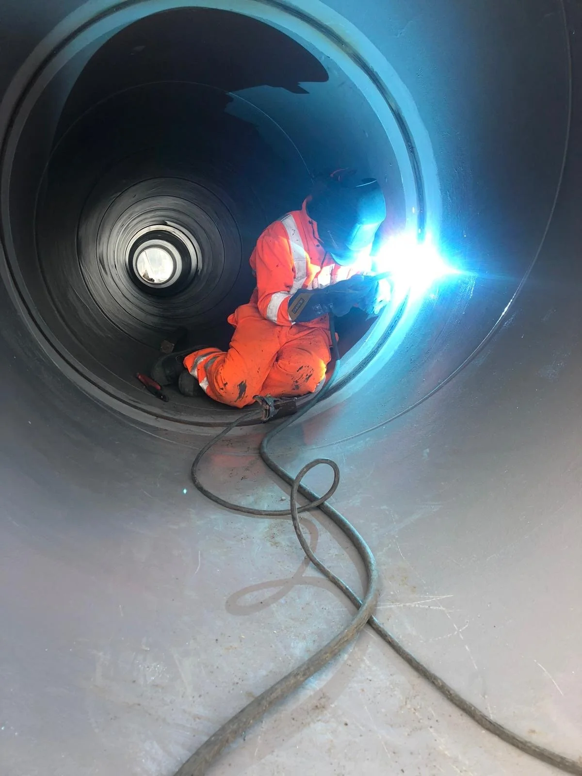Solid Line Fabrication staff in orange safety gear welding inside a large metallic pipe, with bright blue welding sparks.