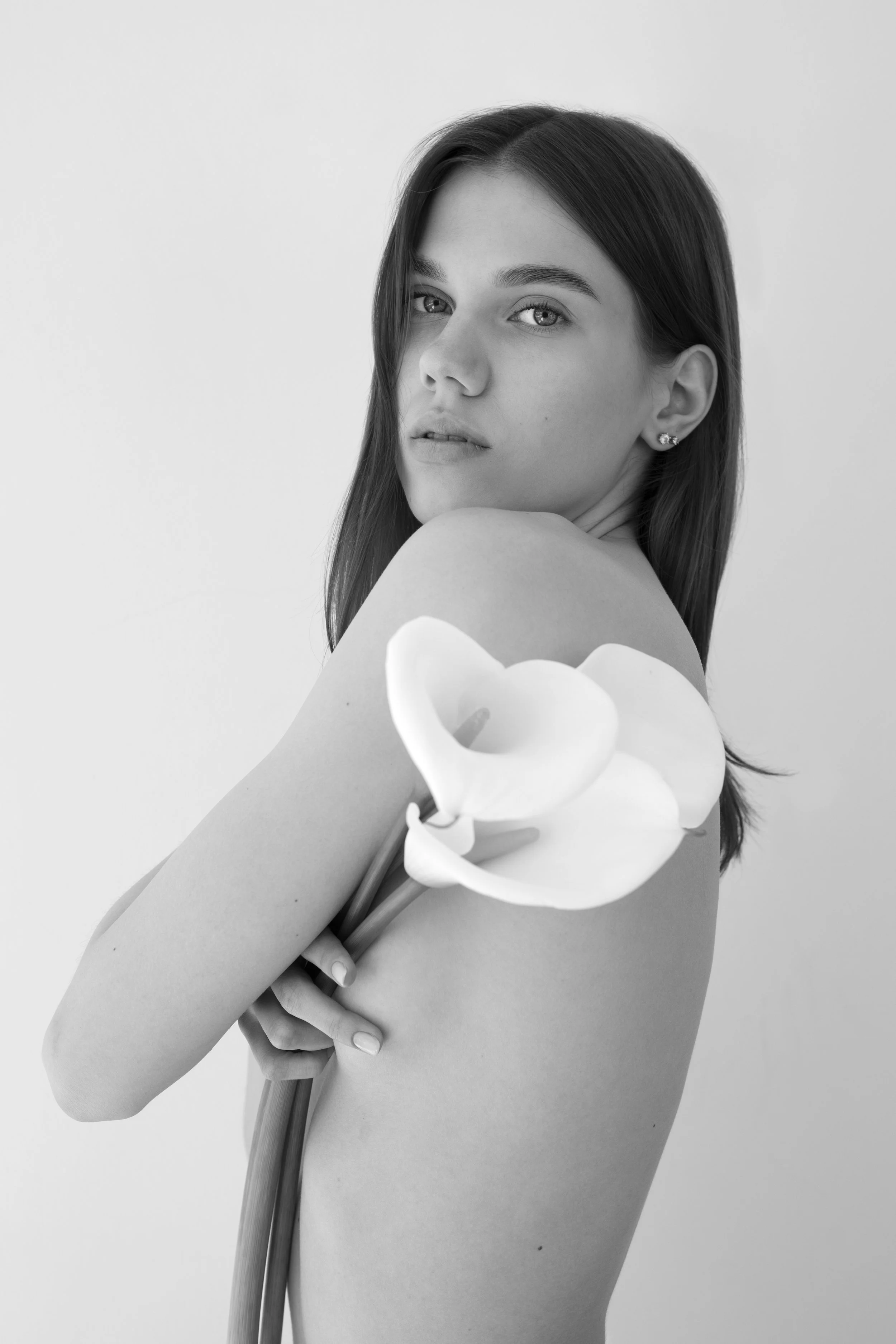 Black and white photo of a woman holding white calla lilies, looking at the camera, with a neutral background.