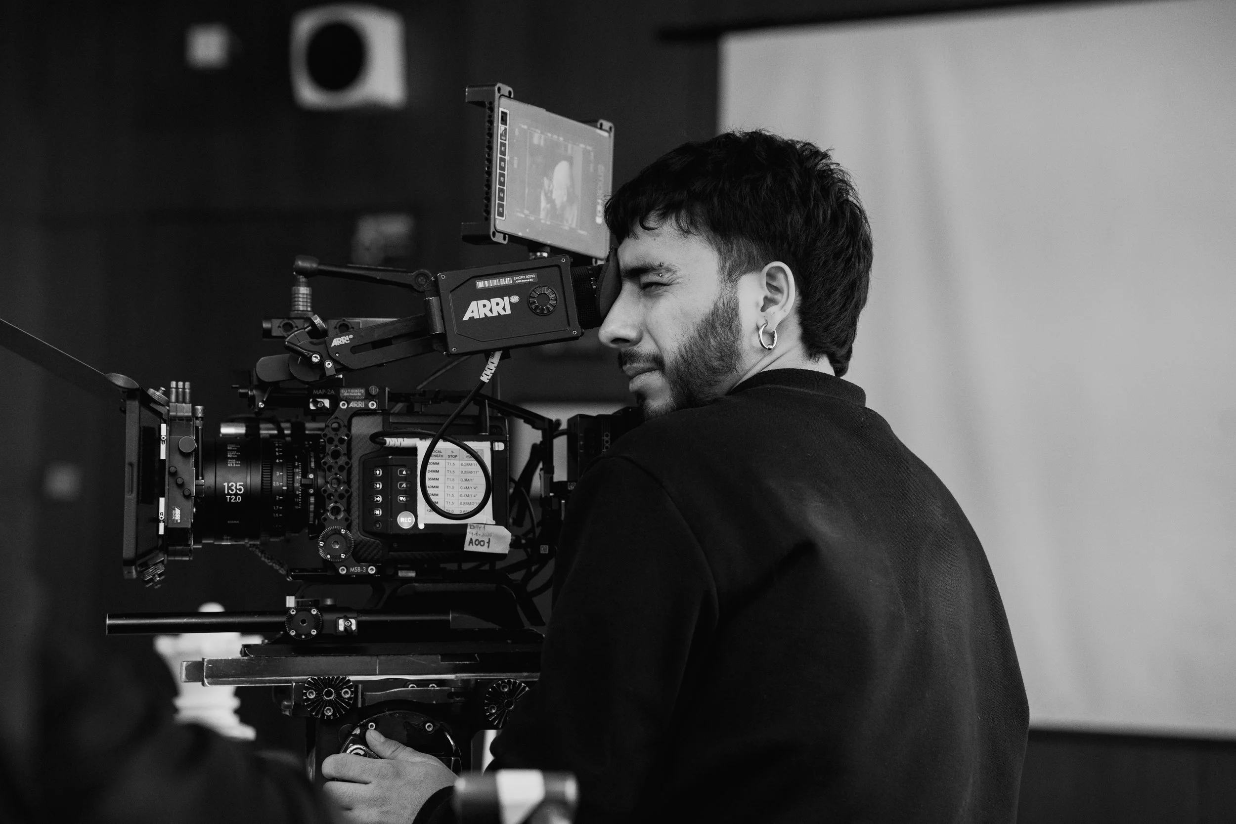 A person with dark hair and earrings operating a professional camera setup on a film or photography set, with a monitor attached to view footage.