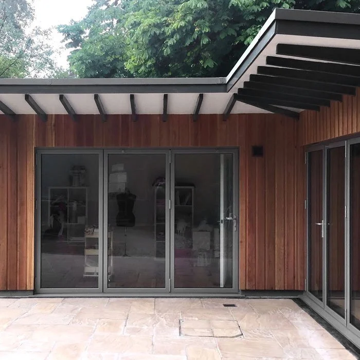 Exterior view of a modern building with wooden siding, sliding glass doors, and a flat roof with overhang.