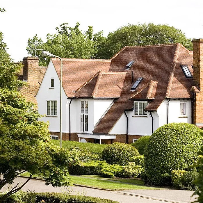 White house with red-tile roof, surrounded by green trees and neatly trimmed bushes.