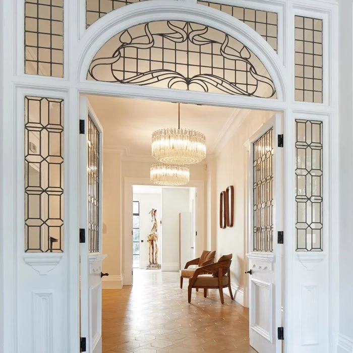 Elegant entryway with decorative glass door, chandelier, and seating area with two armchairs.