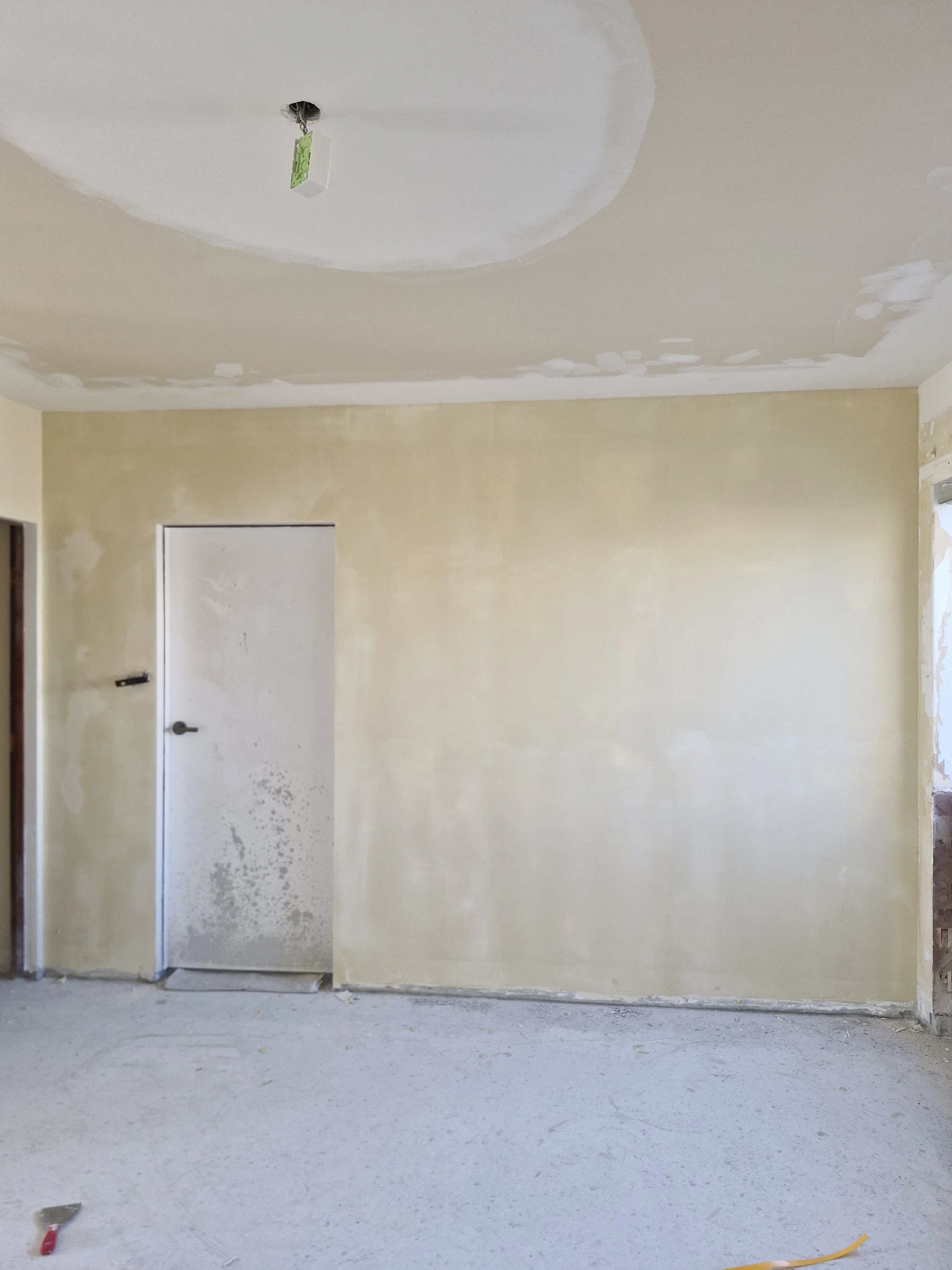 Room under construction with unfinished walls and ceiling, a white door, and construction tools on the floor.