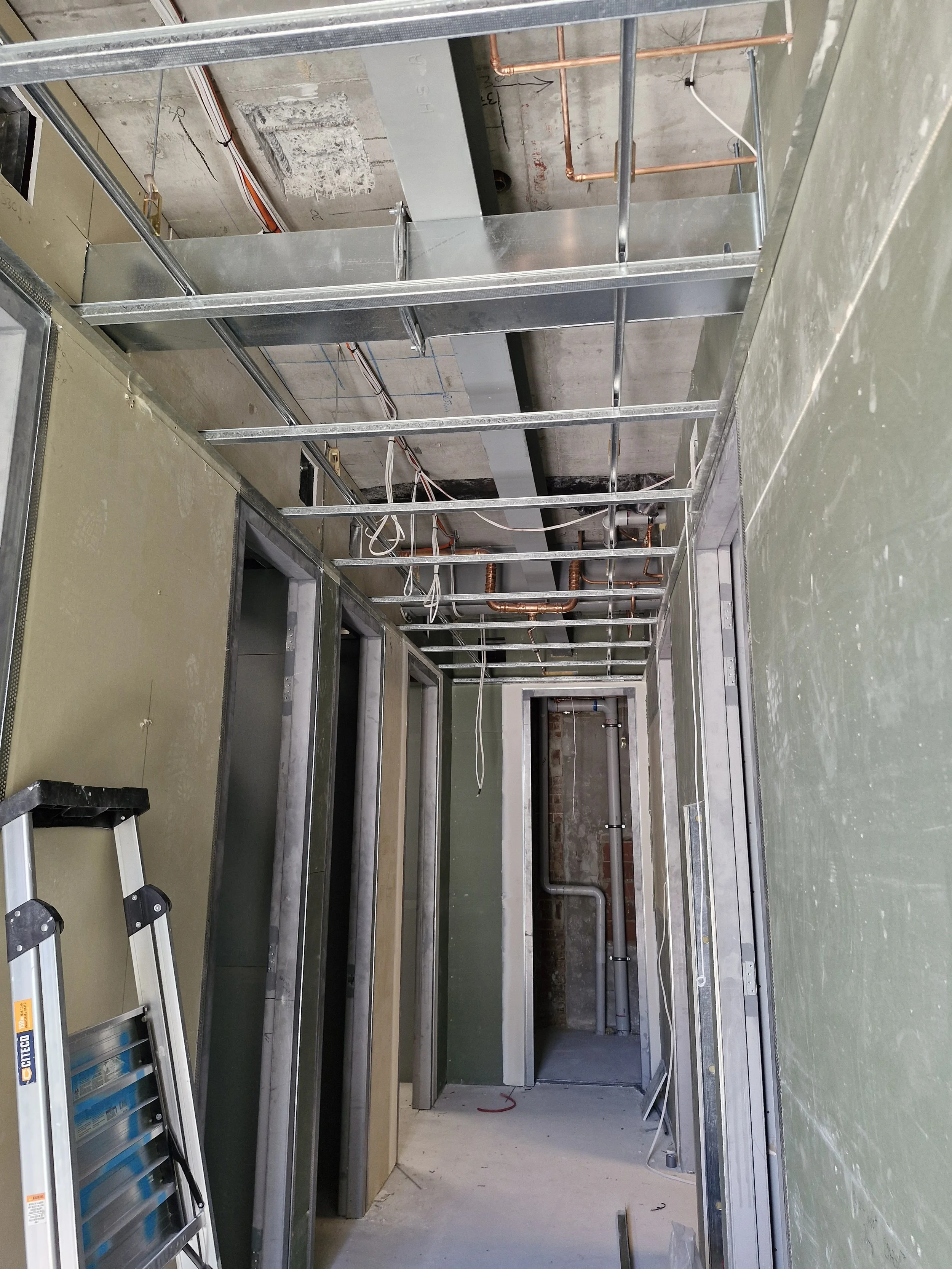 Construction site with metal framing and electrical wiring in progress, doorway openings, ladder leaning against wall.