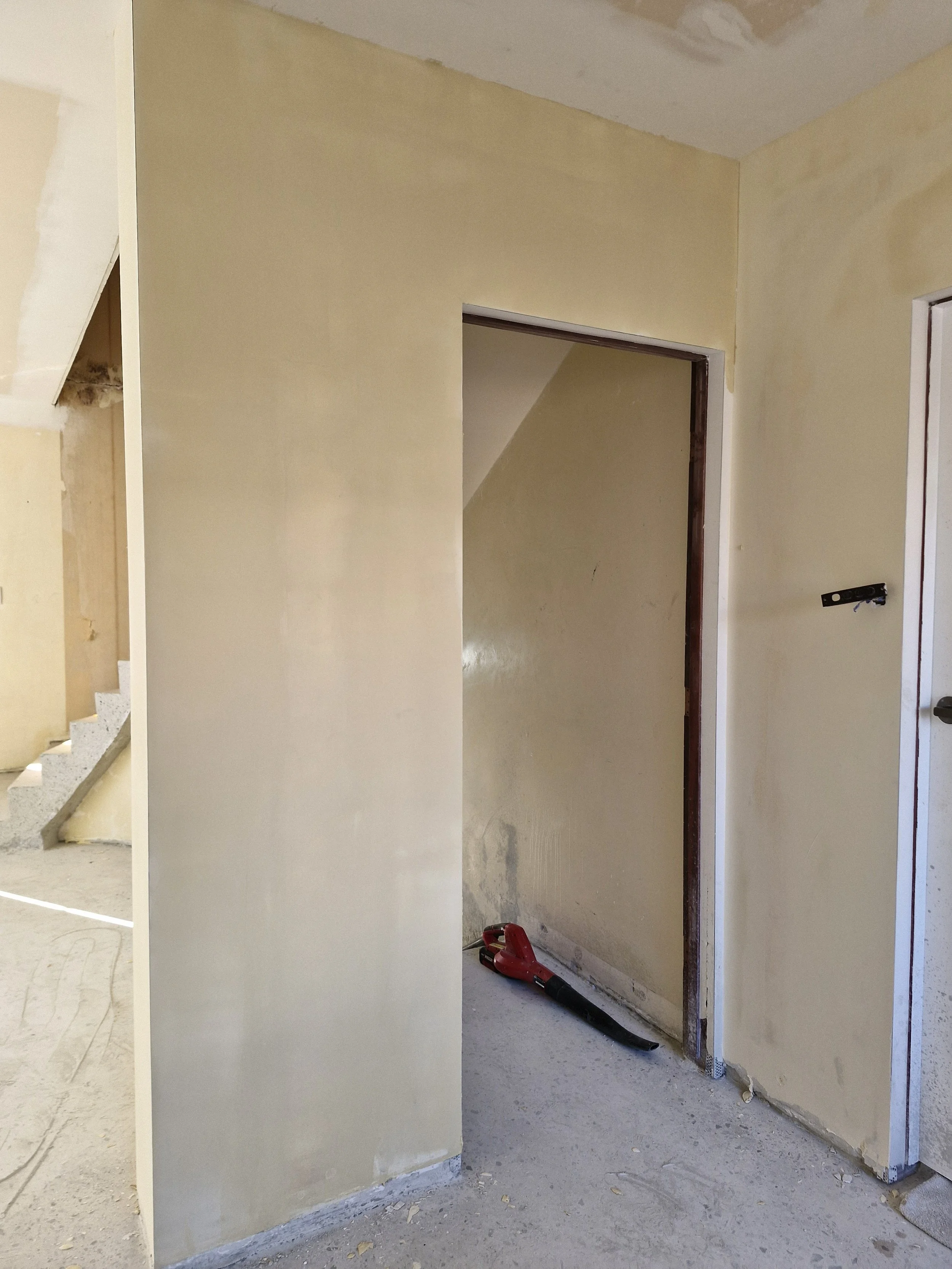 Interior view of a house under renovation with unfinished walls, a door frame, and a construction vacuum on the floor.