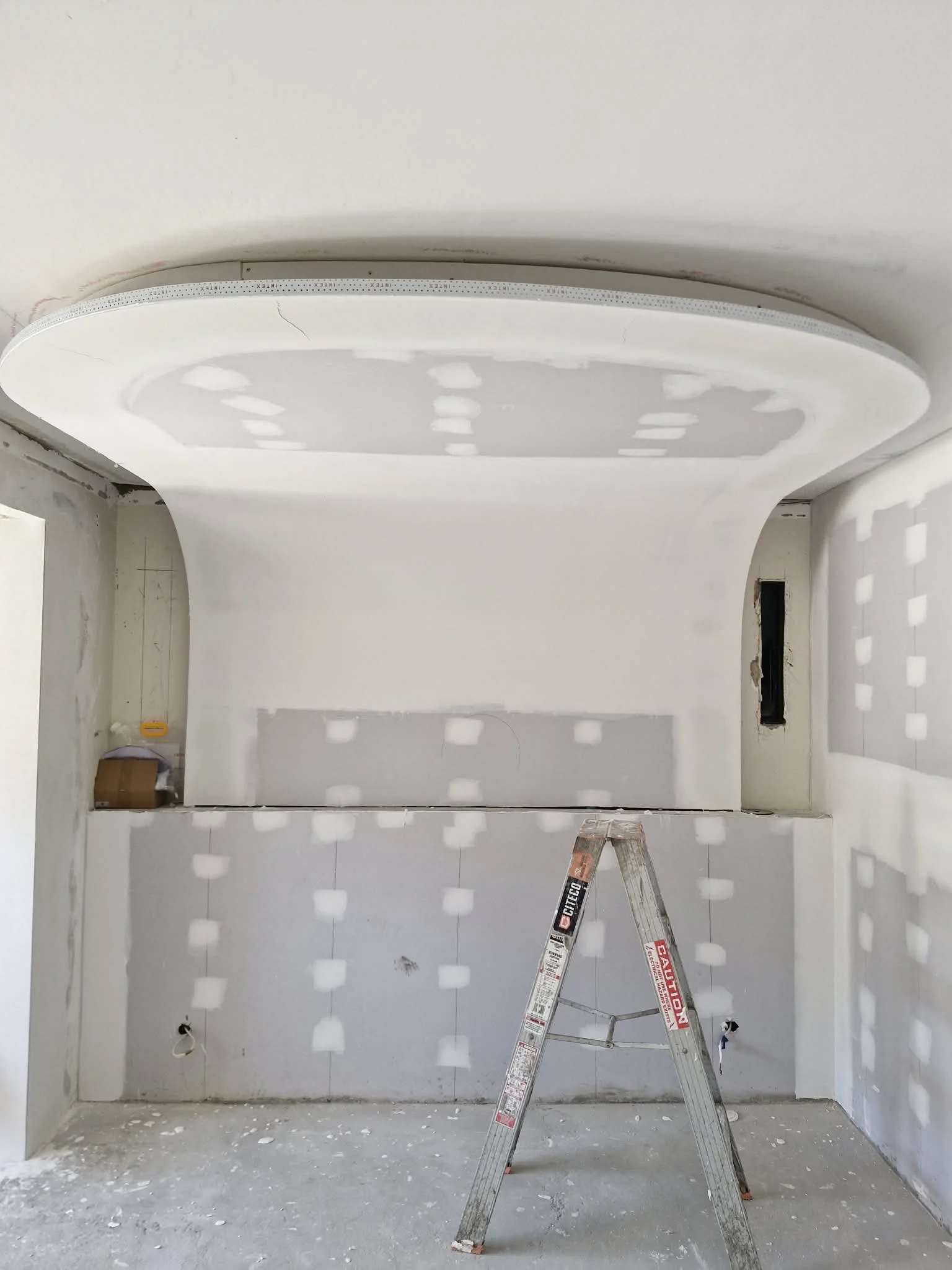 Interior of a room under construction with drywall, curved feature walls, flushing work