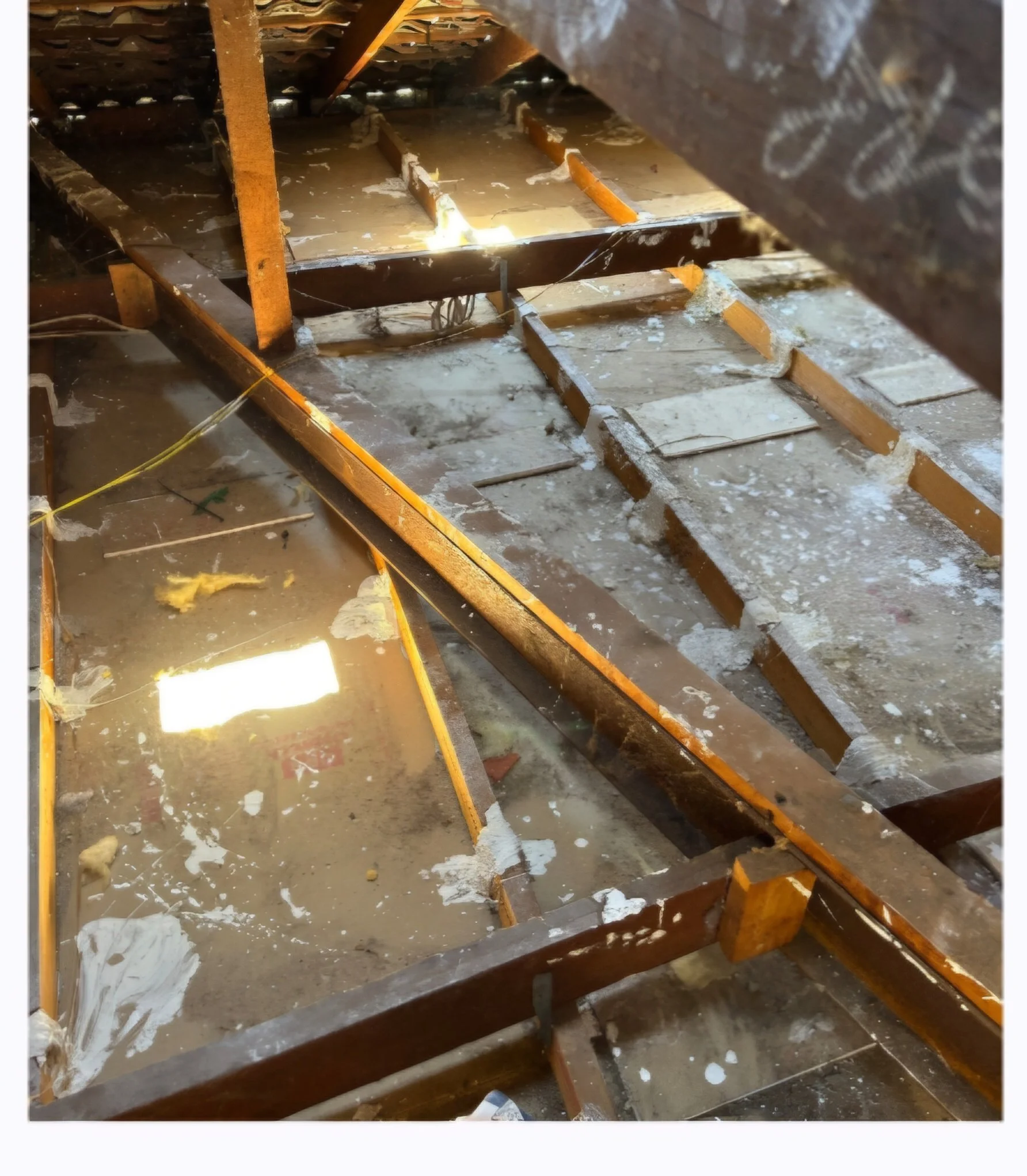 View of a muddy construction site with exposed wooden floor beams, some covered in water and debris, indicating ongoing renovations or damage.