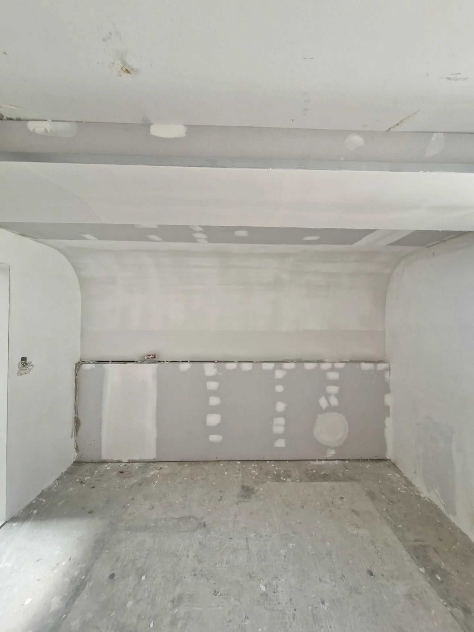 A room under construction with drywall installation and patching in progress, curved feature walls constructed 