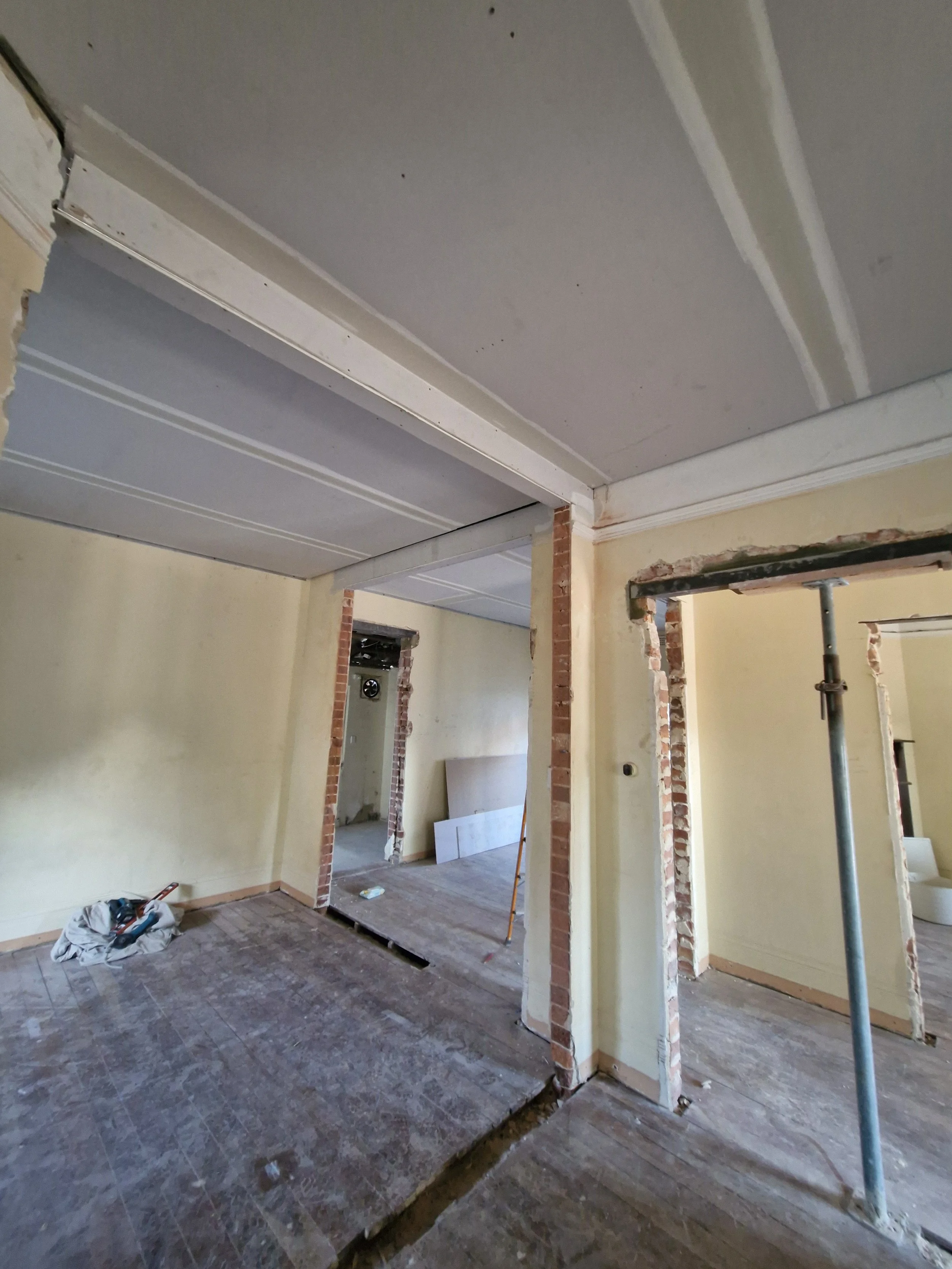 Room under renovation with partially removed walls, exposed brick, construction tools, and drywall.