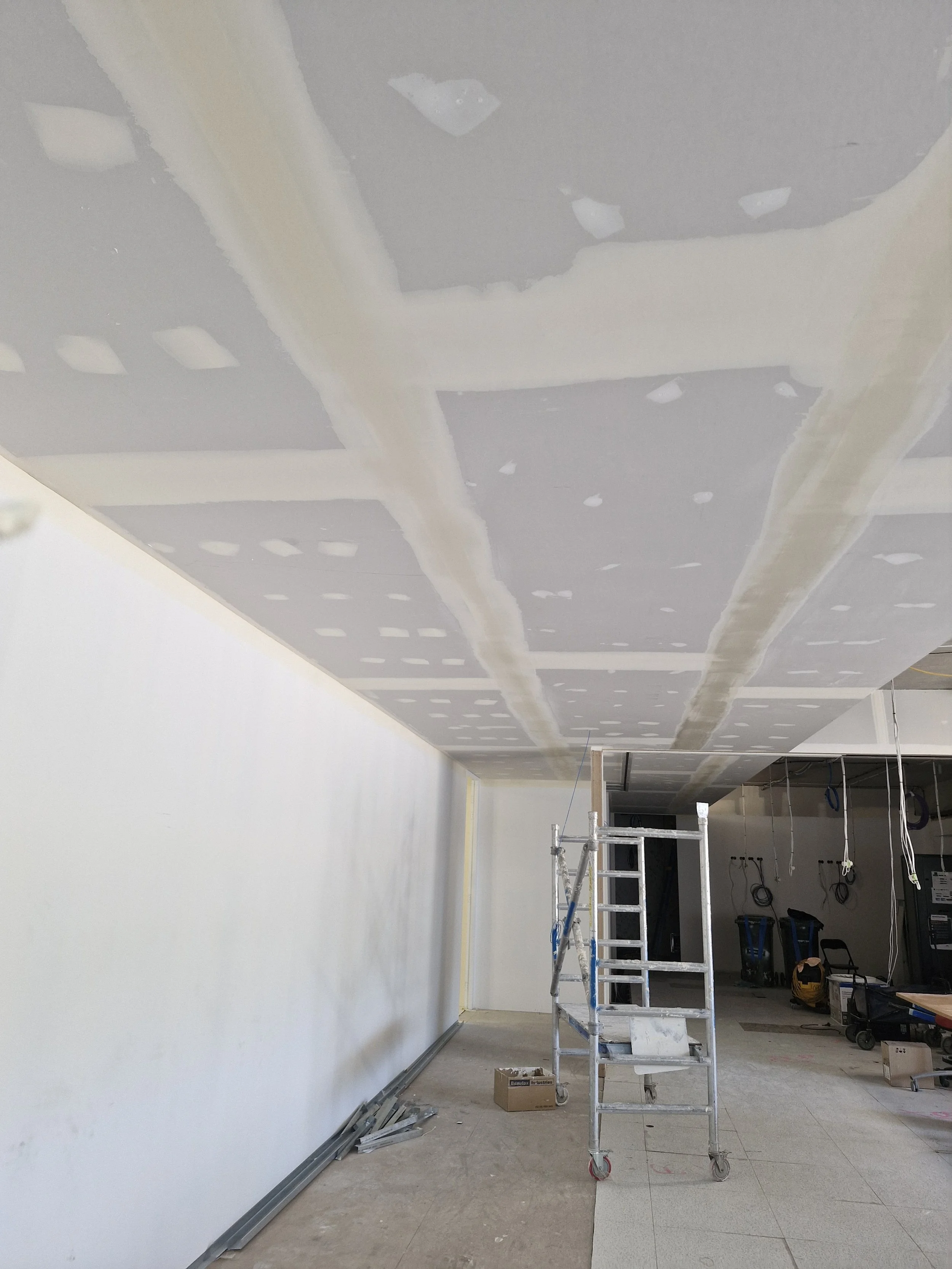 Construction site with unfinished ceiling, ladder, tools, and materials.