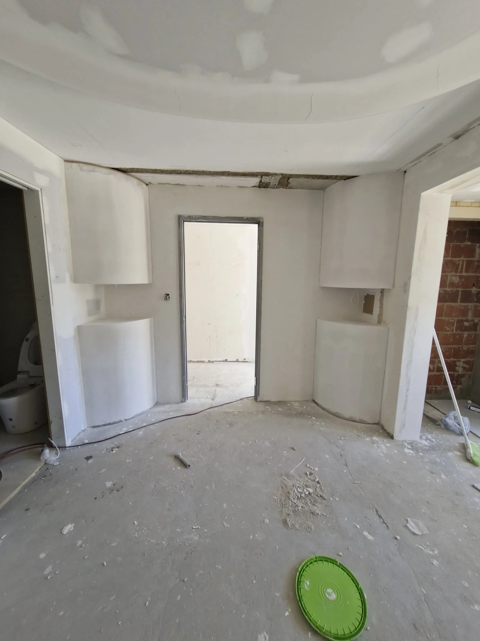 Interior of a room under construction with drywall walls, a partially finished ceiling, curved feature walls, flushing, drywall