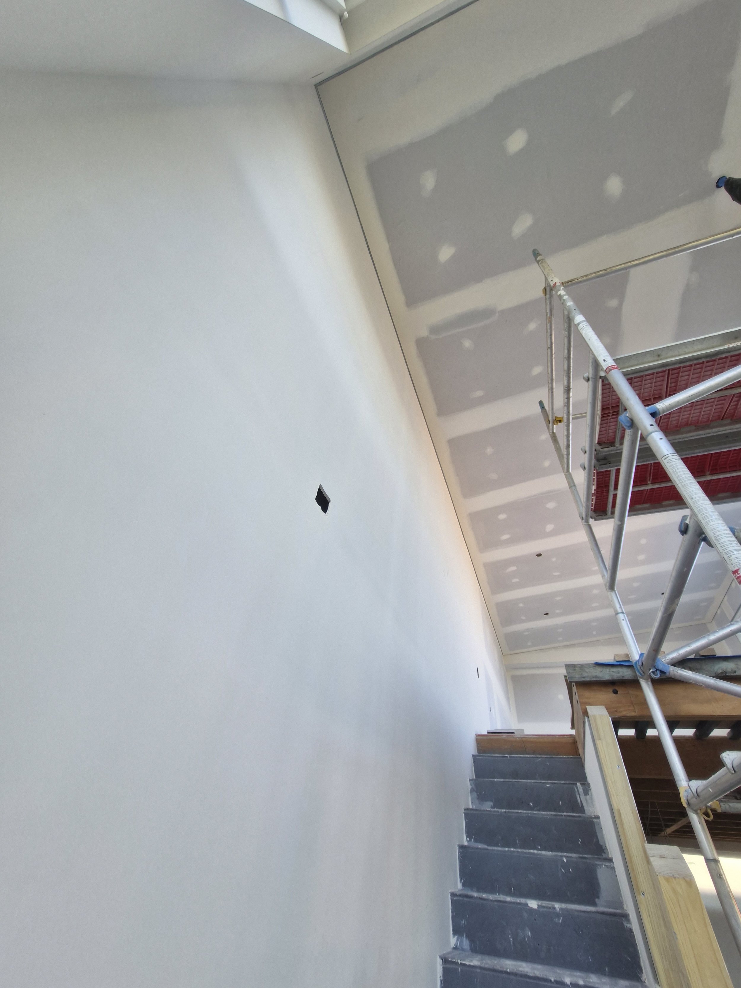 Interior wall under construction with drywall and scaffolding, staircase at the bottom right.