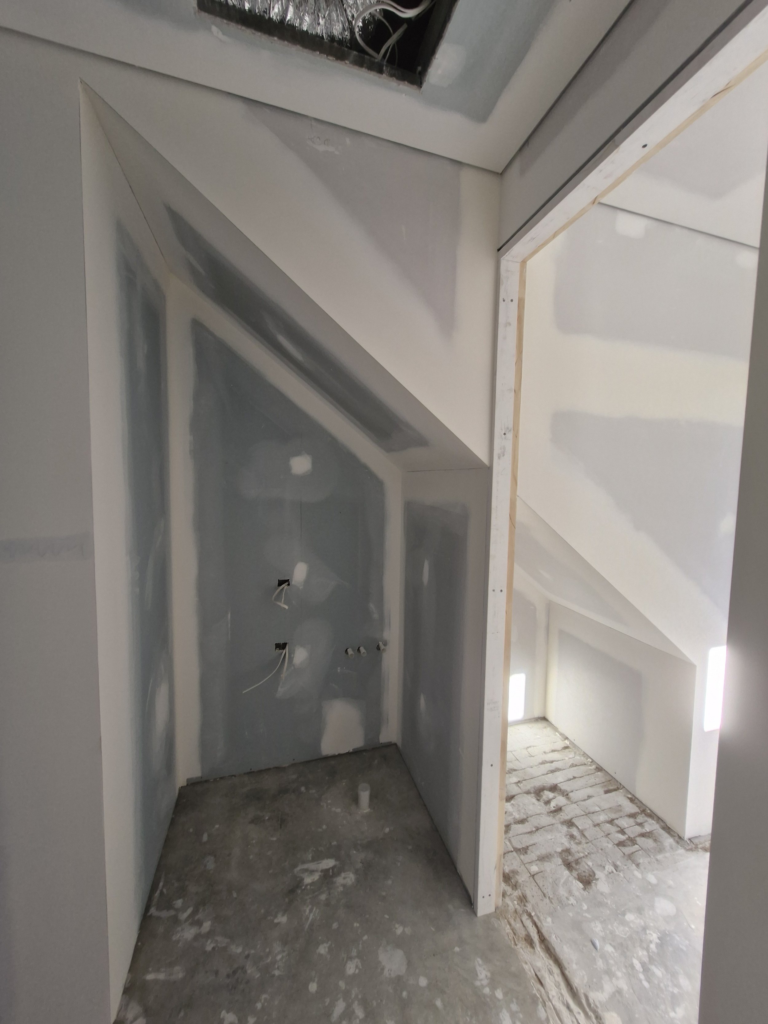 Interior view of a finished room with drywall installation, electrical wiring, and a sloped ceiling, possibly in a house under construction.