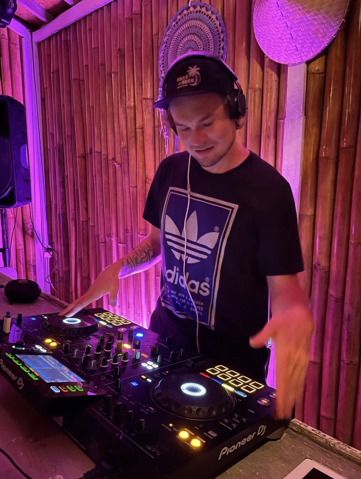 DJ soittaa musiikkia klubissa tai tapahtumassa, taustalla bambu-seinä ja vesi- ja auringonlaskiteemainen sisustus.