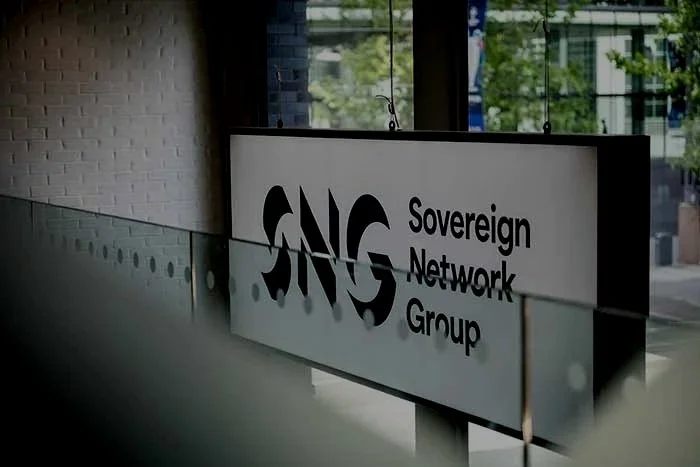 A sign with the logo and text for SNG Sovereign Network Group, hanging inside a building near a glass window.