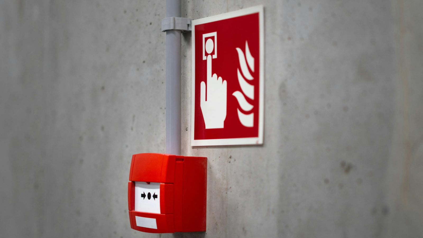 Fire alarm pull station below a red fire safety sign on a concrete wall.
