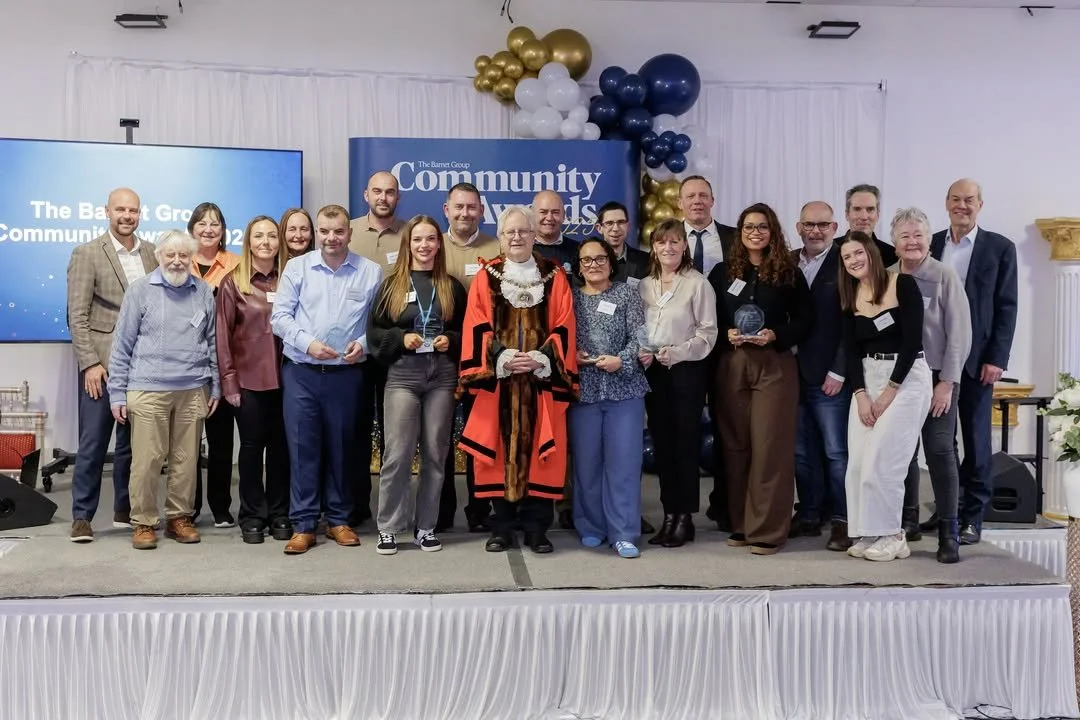 Group of people on stage at the Barnet Group Community Awards event, with a backdrop displaying the event name and balloons in the background.