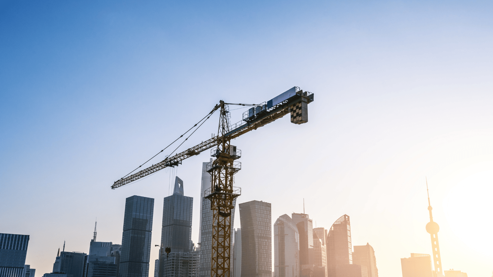 Construction crane over a city skyline with tall buildings and a clear sky.