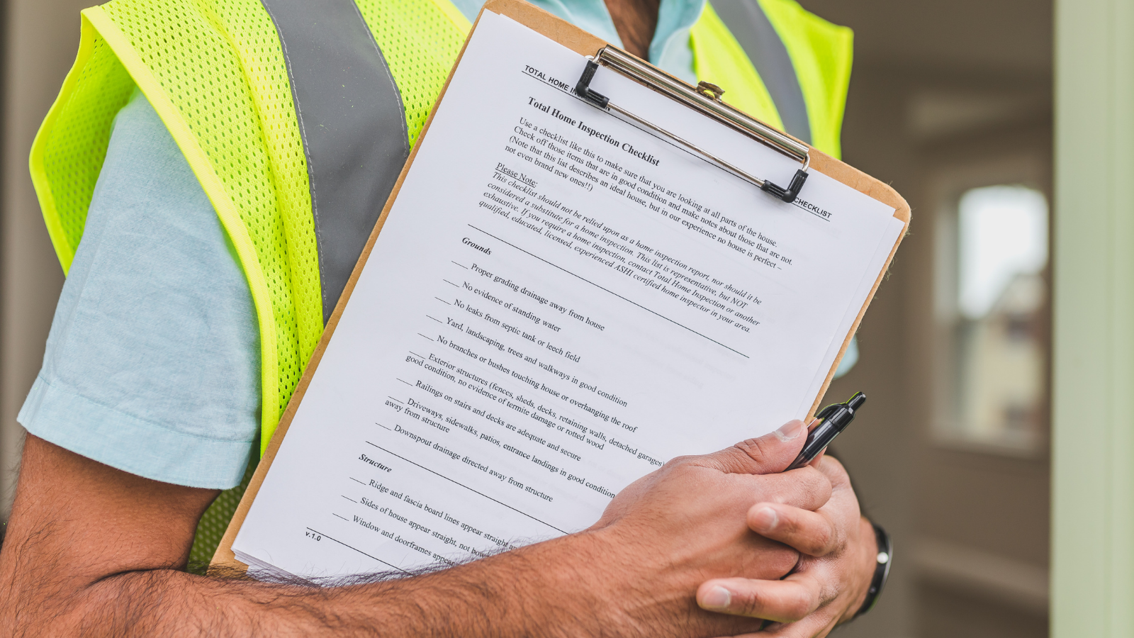 A person wearing a yellow safety vest holding a clipboard with a home inspection checklist.