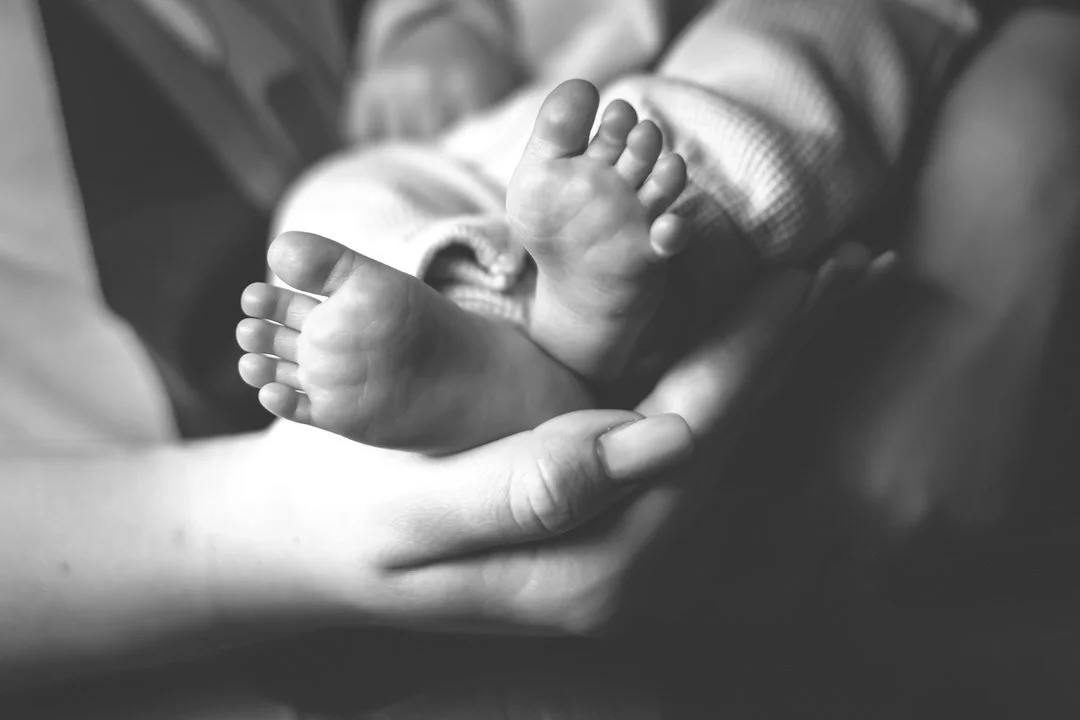 A mother holding a baby's feet with one hand, the baby is lying on their back, in black and white.